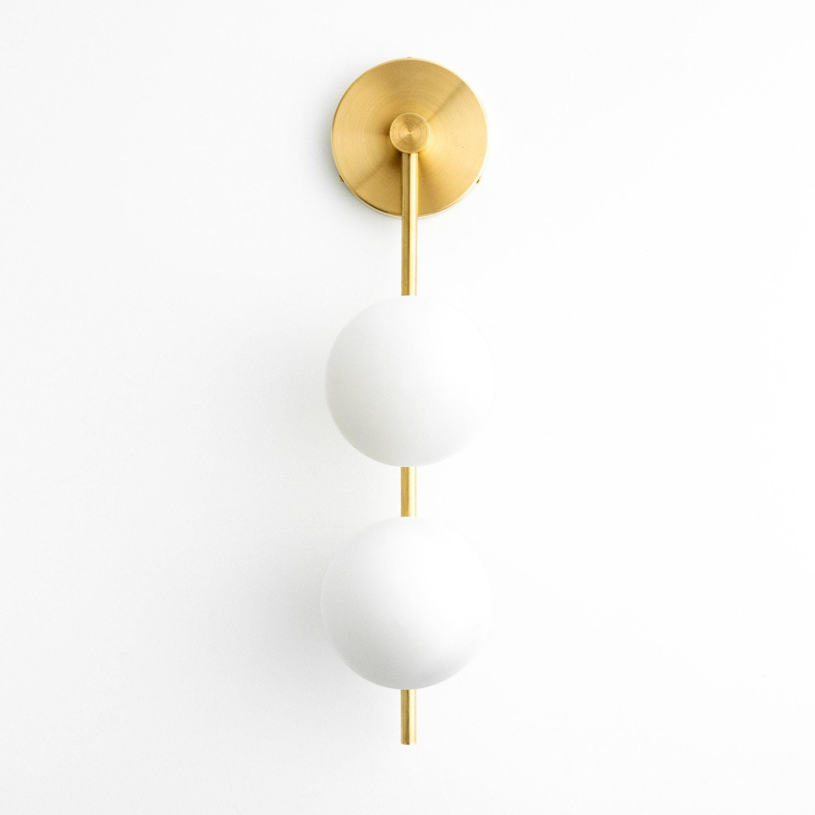 Modern wall sconce with two white globe lights and a slim brass rod mounting on a round brass base. - SCONCE MODEL NO. 0344