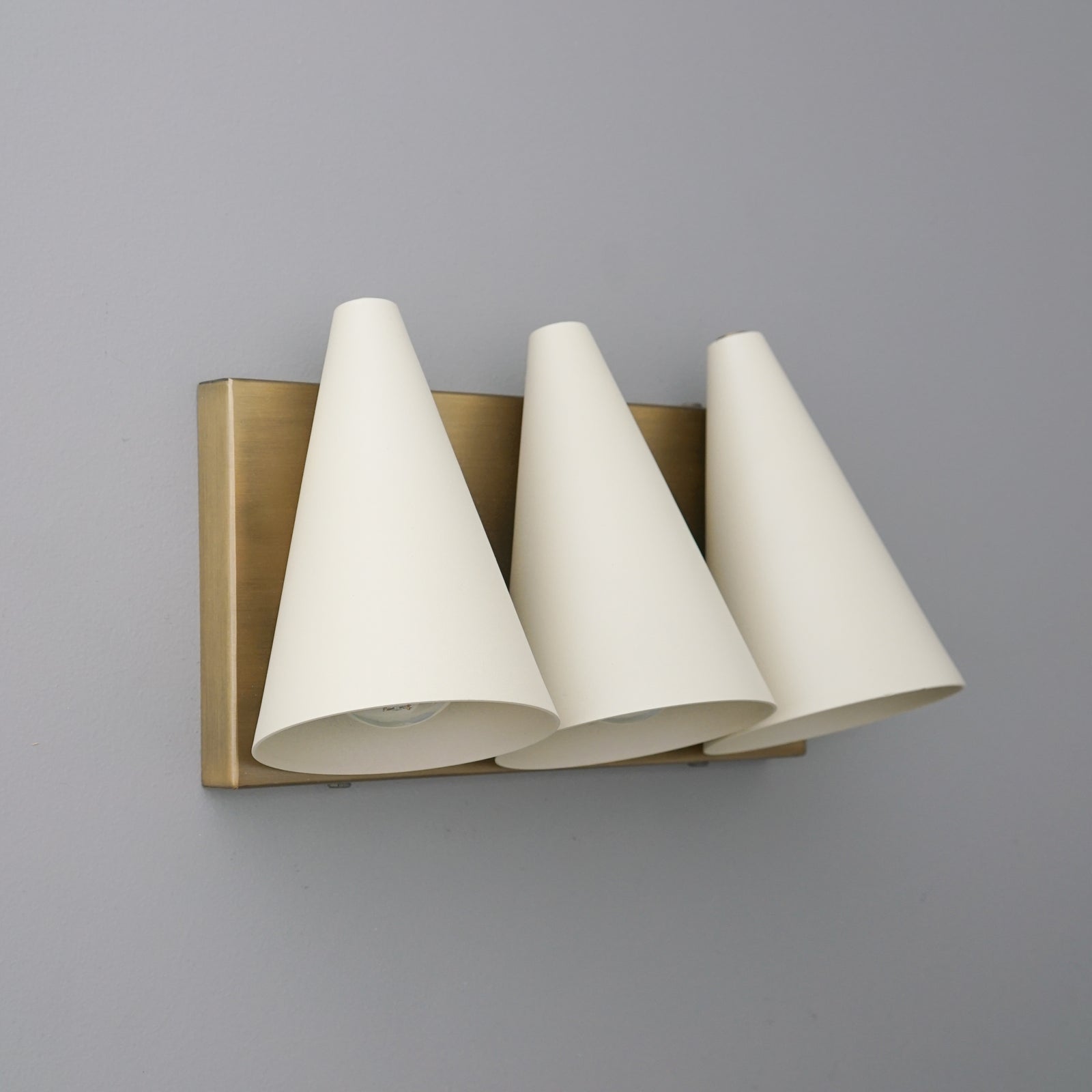 Three-cone-shaped white shades mounted on brushed gold rectangular base vanity light fixture. - VANITY MODEL NO. 2330