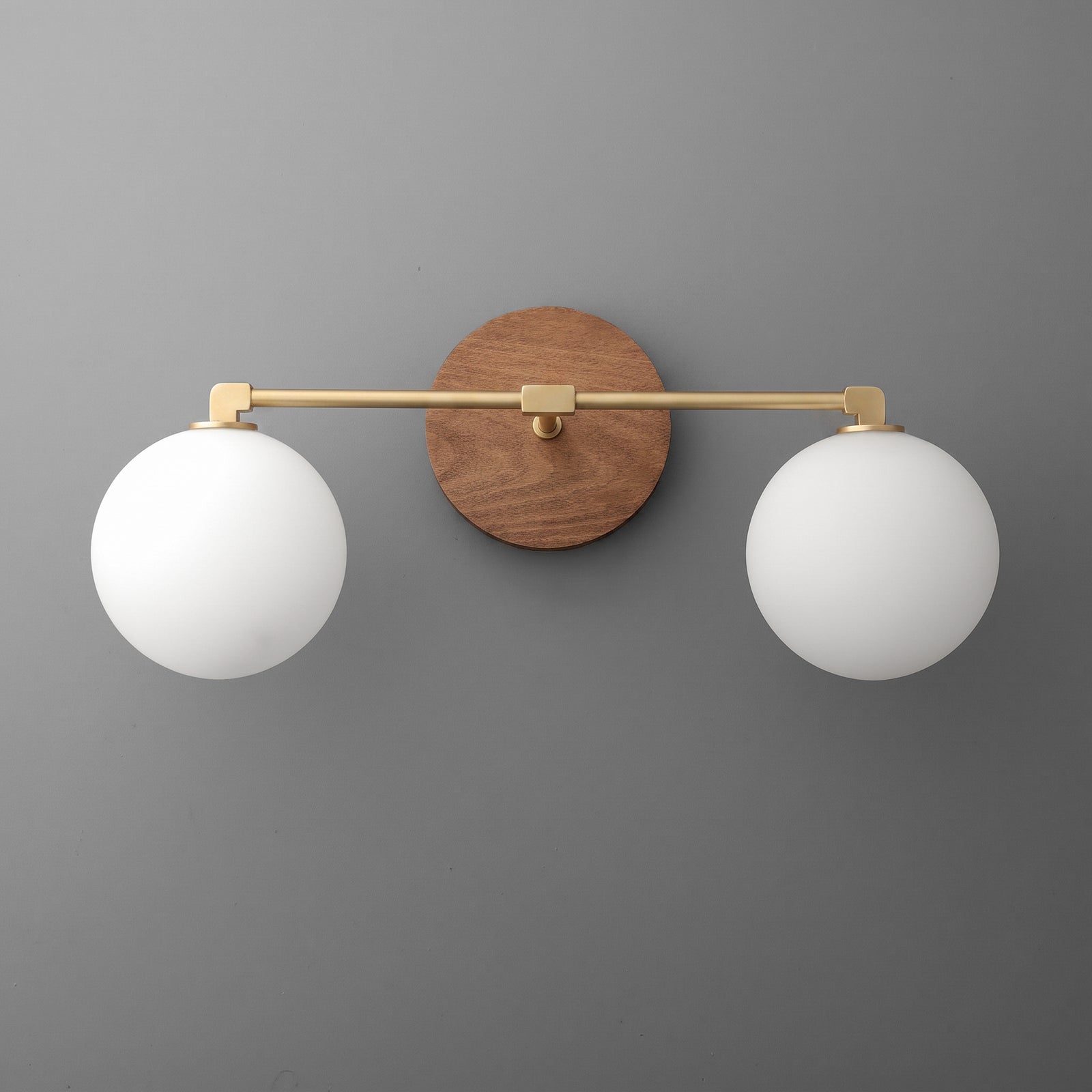 Wall-mounted vanity light with two white frosted glass globes, brass horizontal bar, and round wood backplate. - VANITY LIGHT MODEL NO. 1151