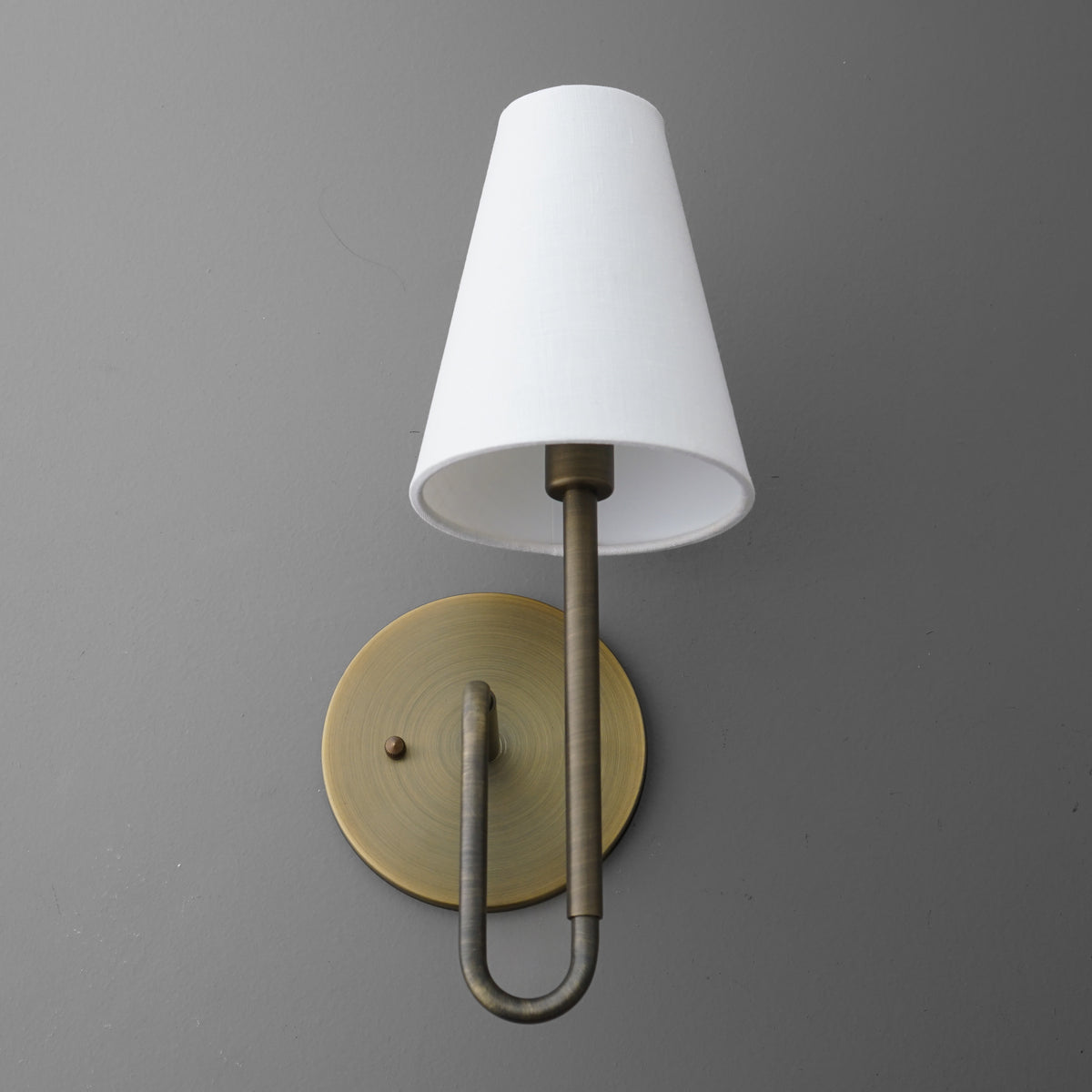 Wall sconce with antique brass finish, curved arm, and white tapered fabric shade. - SCONCE MODEL NO. 1008