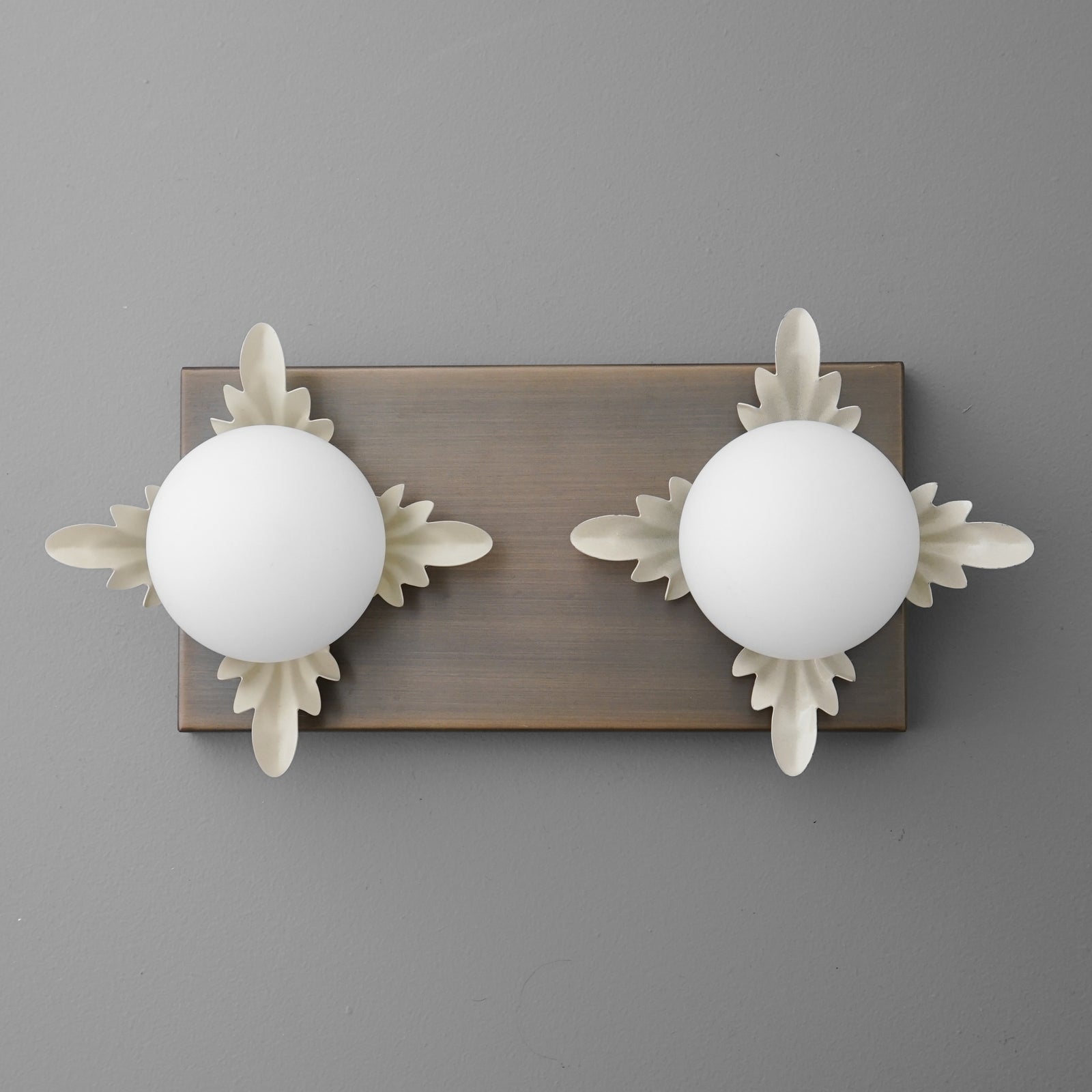 Two-bulb wall sconce with frosted white globes and decorative beige leaf accents on a rectangular bronze backplate. - SCONCE MODEL NO. 1114