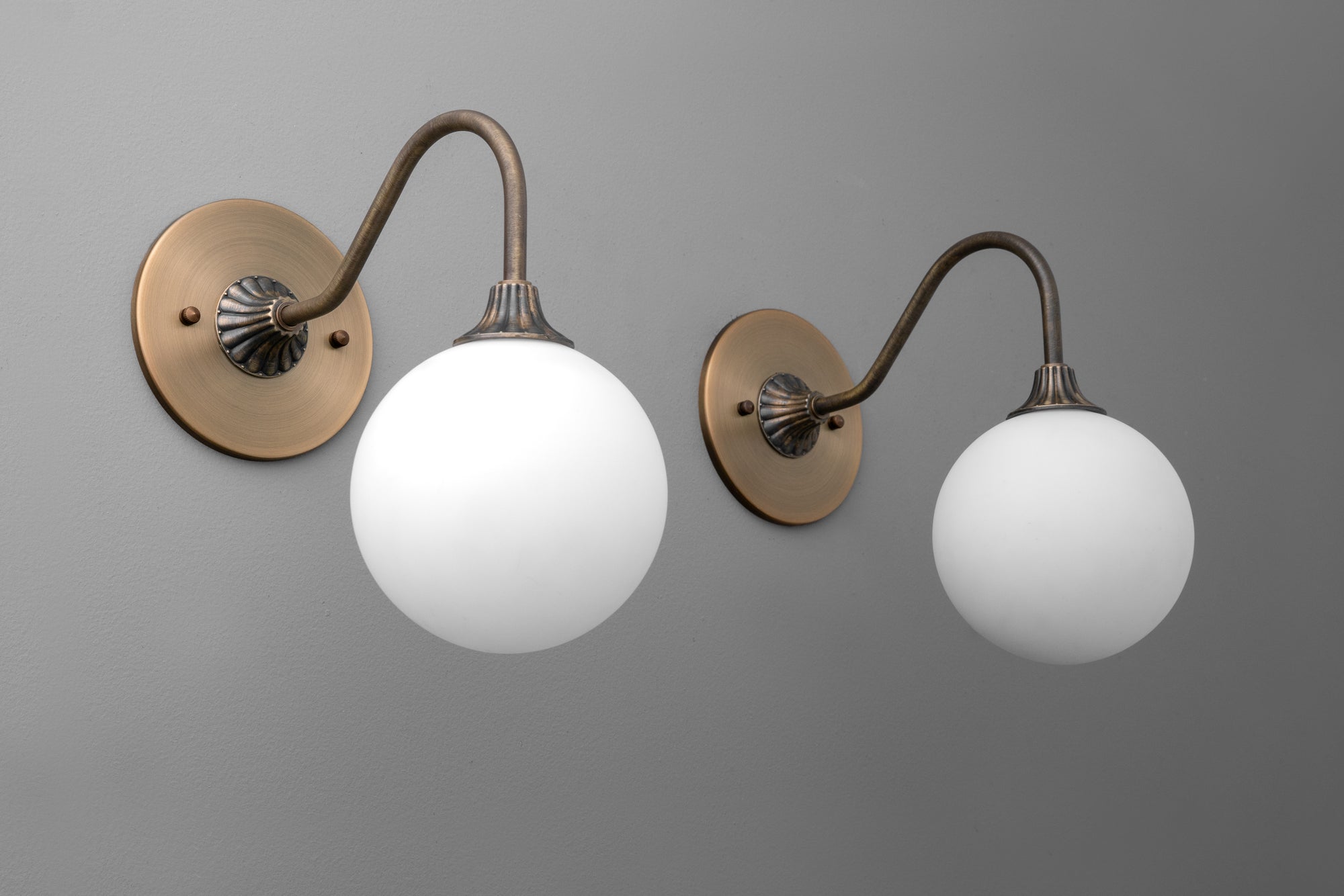 Pair of antique brass wall sconces with curved arms and round white glass globes. - SCONCE MODEL NO. 8263