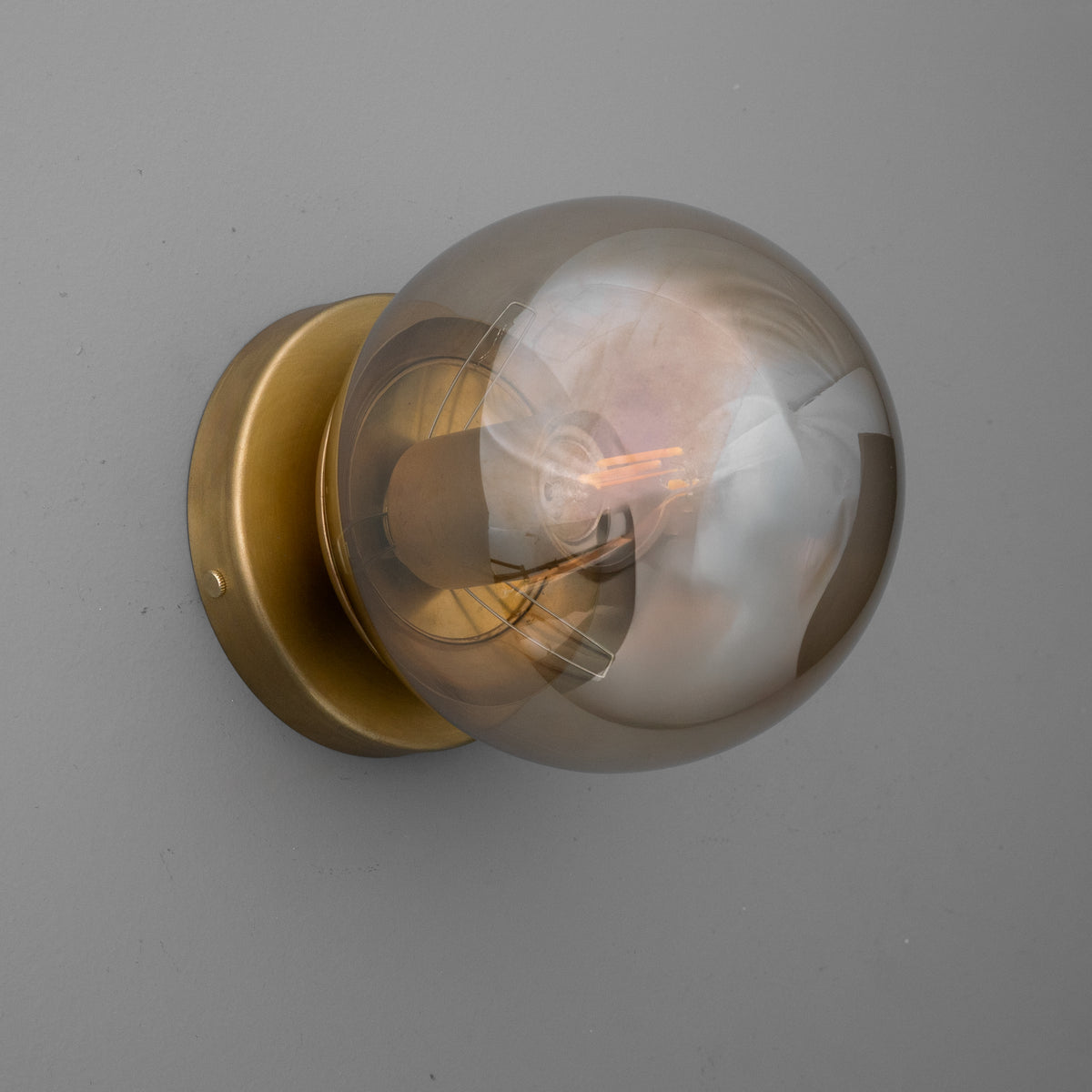 Wall-mounted sconce with a round smoky glass globe and a brass-finished metal base. - SCONCE MODEL NO. 1030