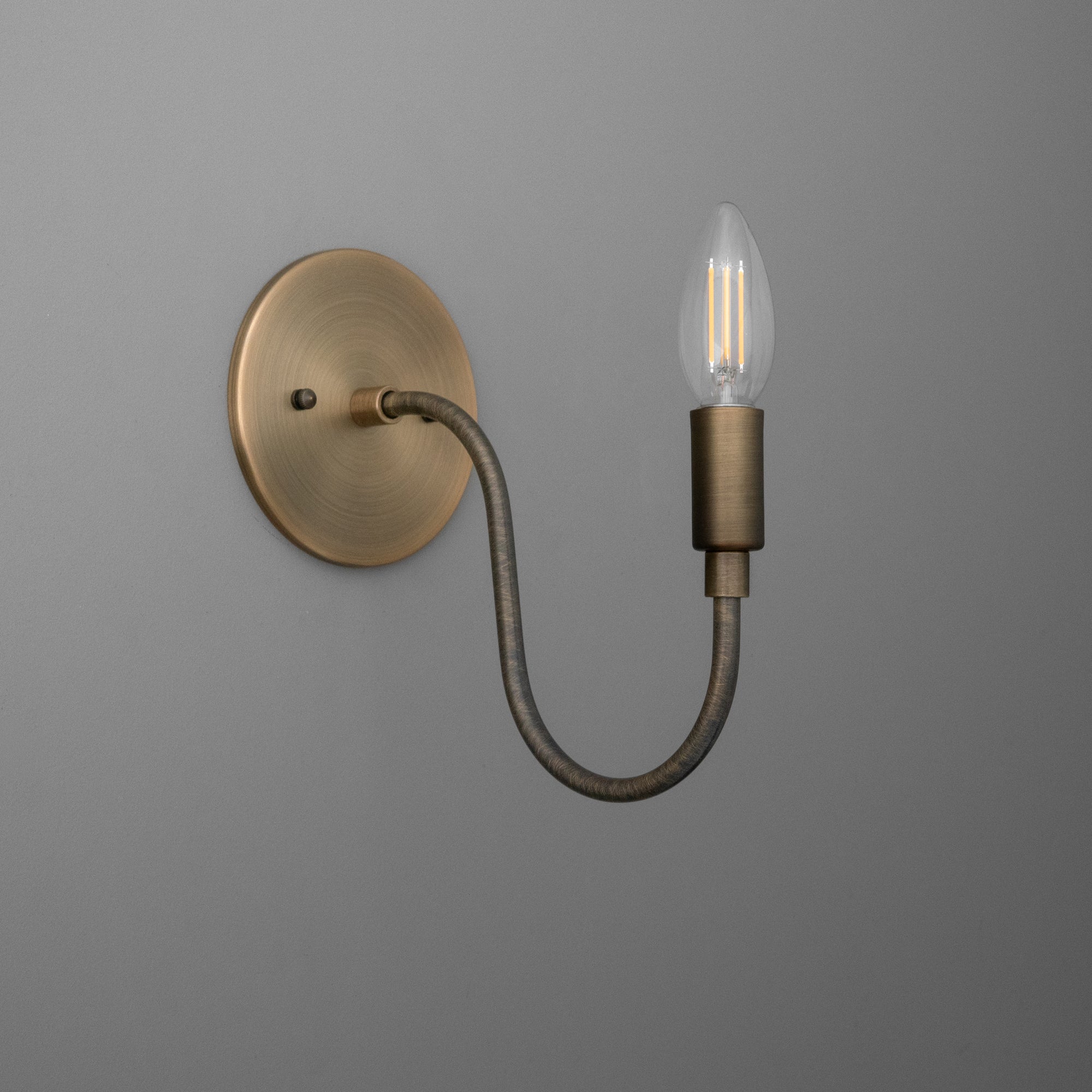 Wall sconce with antique brass finish, curved arm, and exposed vintage-style bulb. - SCONCE MODEL NO. 7321