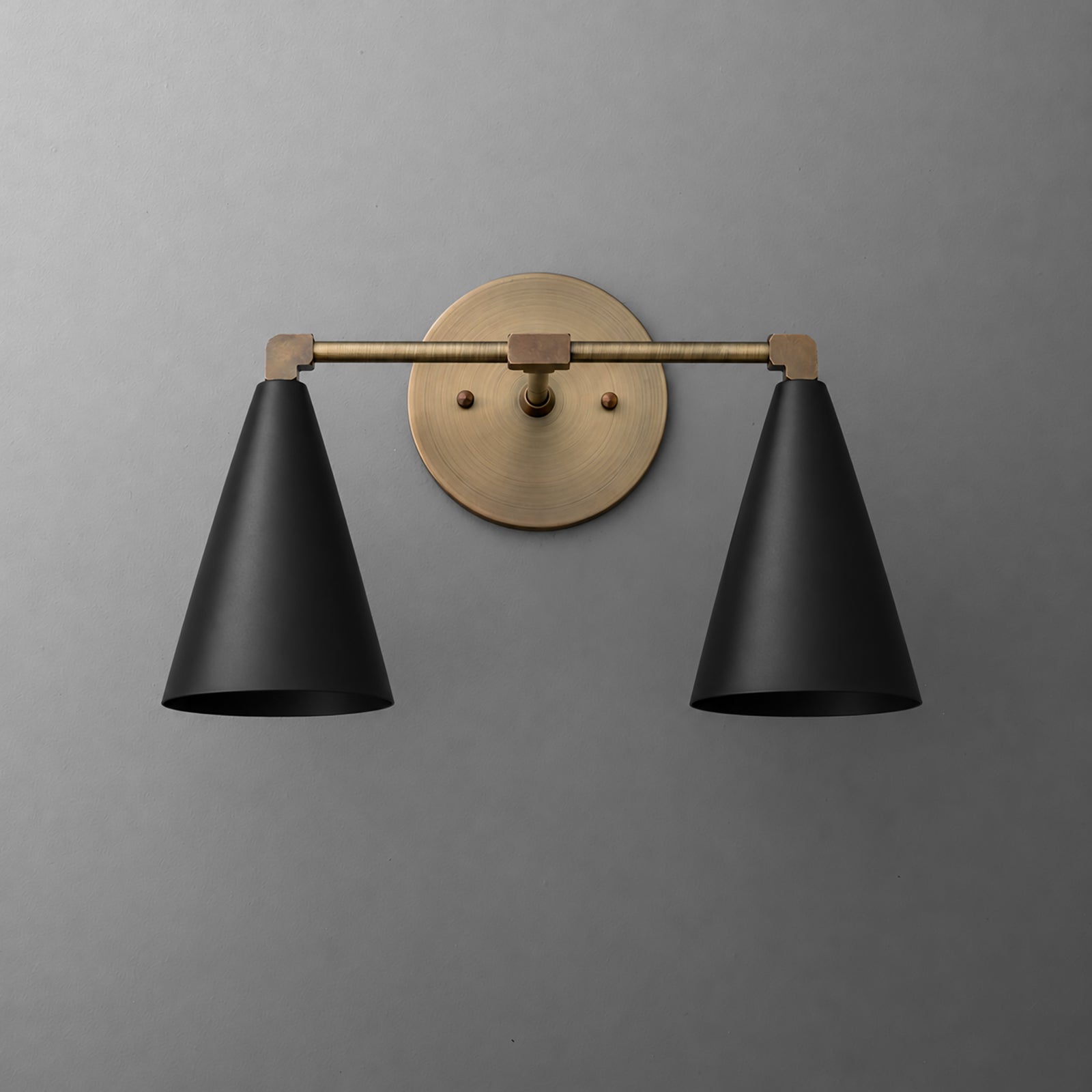 Two-light vanity light in Antique Brass with Black cone shades on a straight arm and a round wall plate. - VANITY LIGHT MODEL NO. 1184