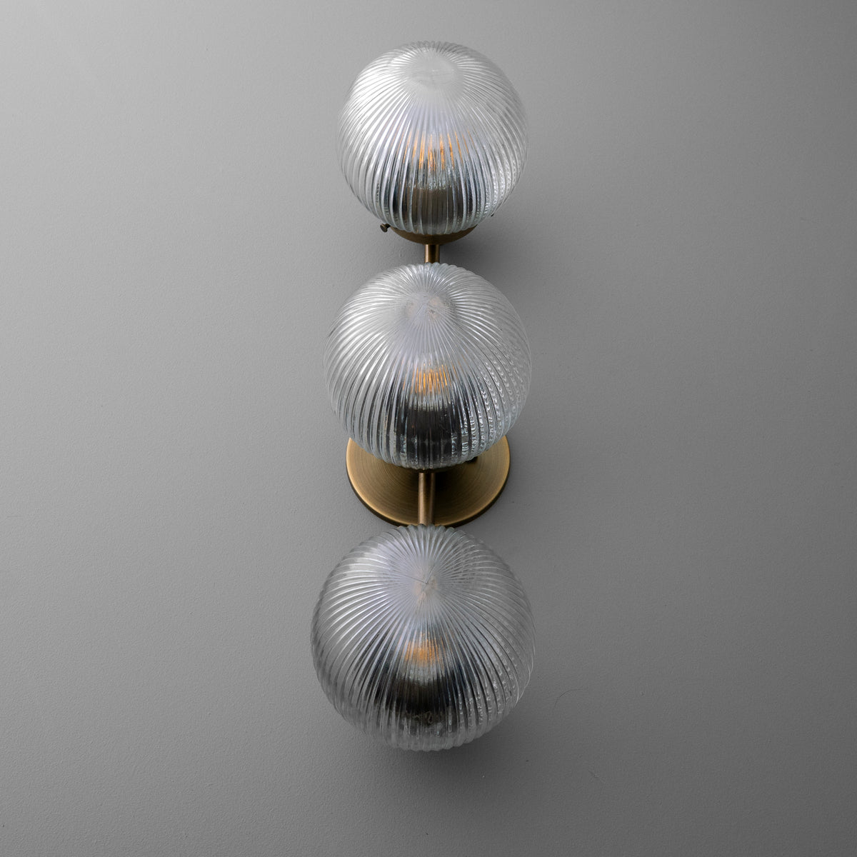 Three-bulb wall sconce with ribbed clear glass globes and a vertical brass mounting plate. - SCONCE MODEL NO. 1108