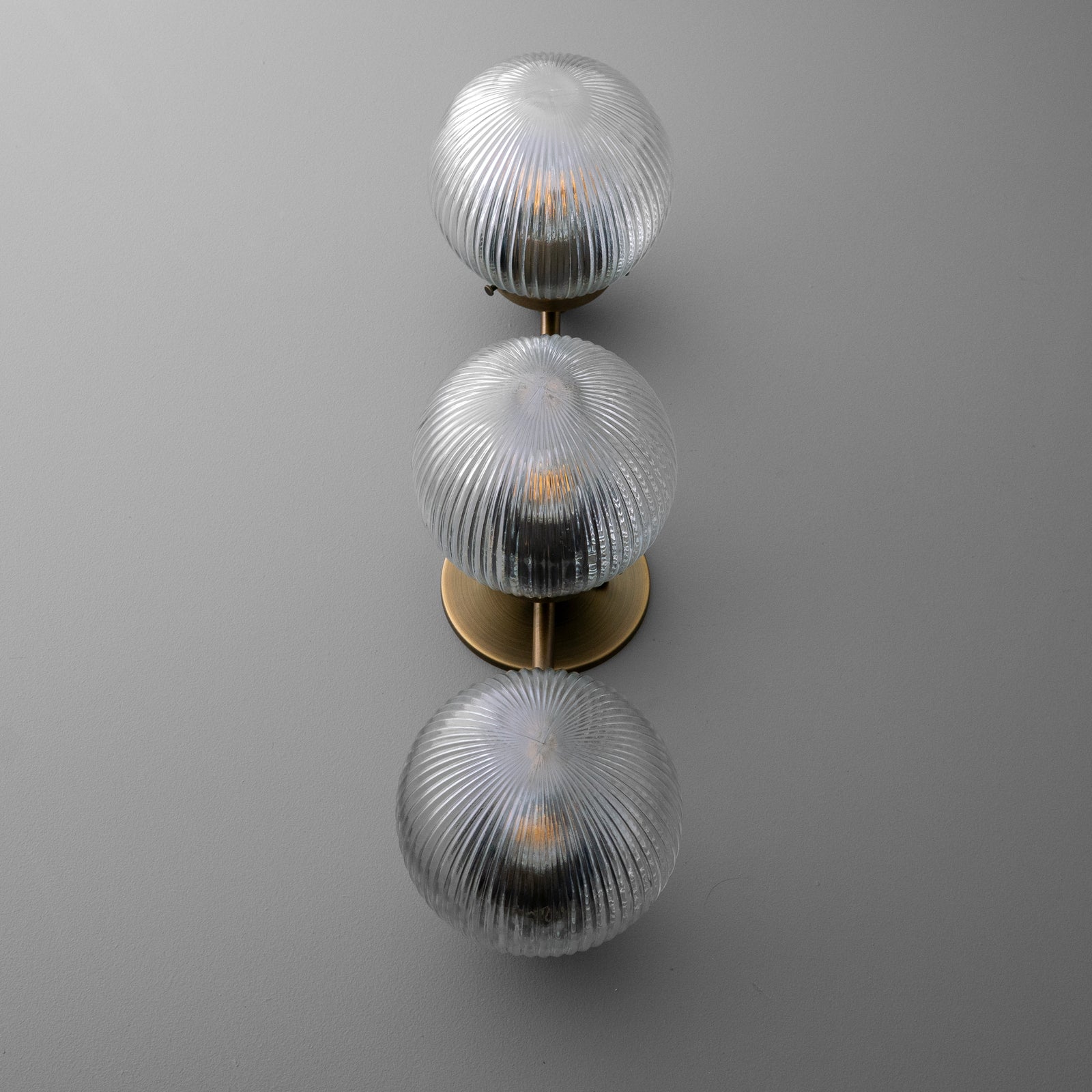 Three-bulb wall sconce with ribbed clear glass globes and a vertical brass mounting plate. - SCONCE MODEL NO. 1108