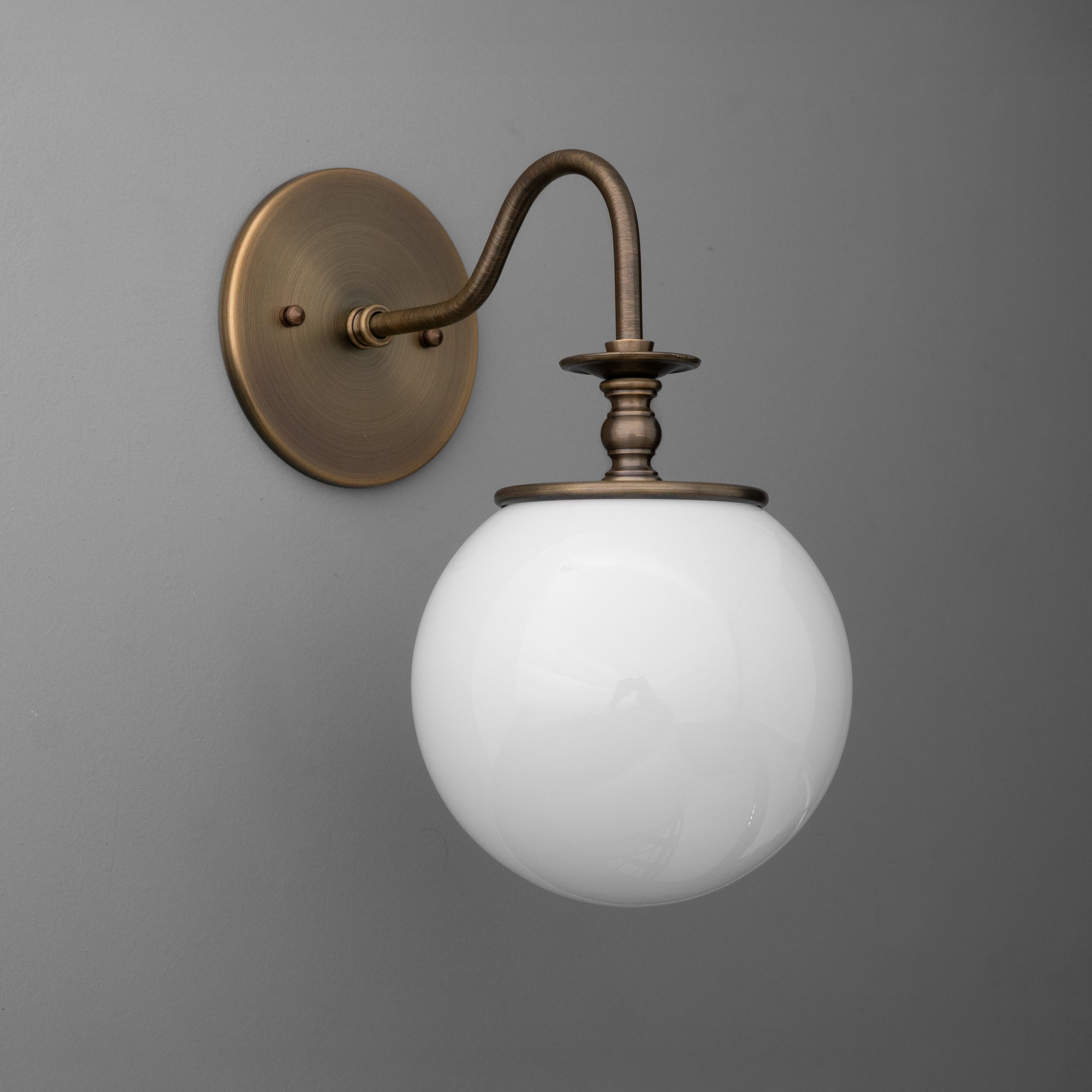 Antique brass wall sconce with curved arm and frosted white glass globe shade. - SCONCE MODEL NO. 7857