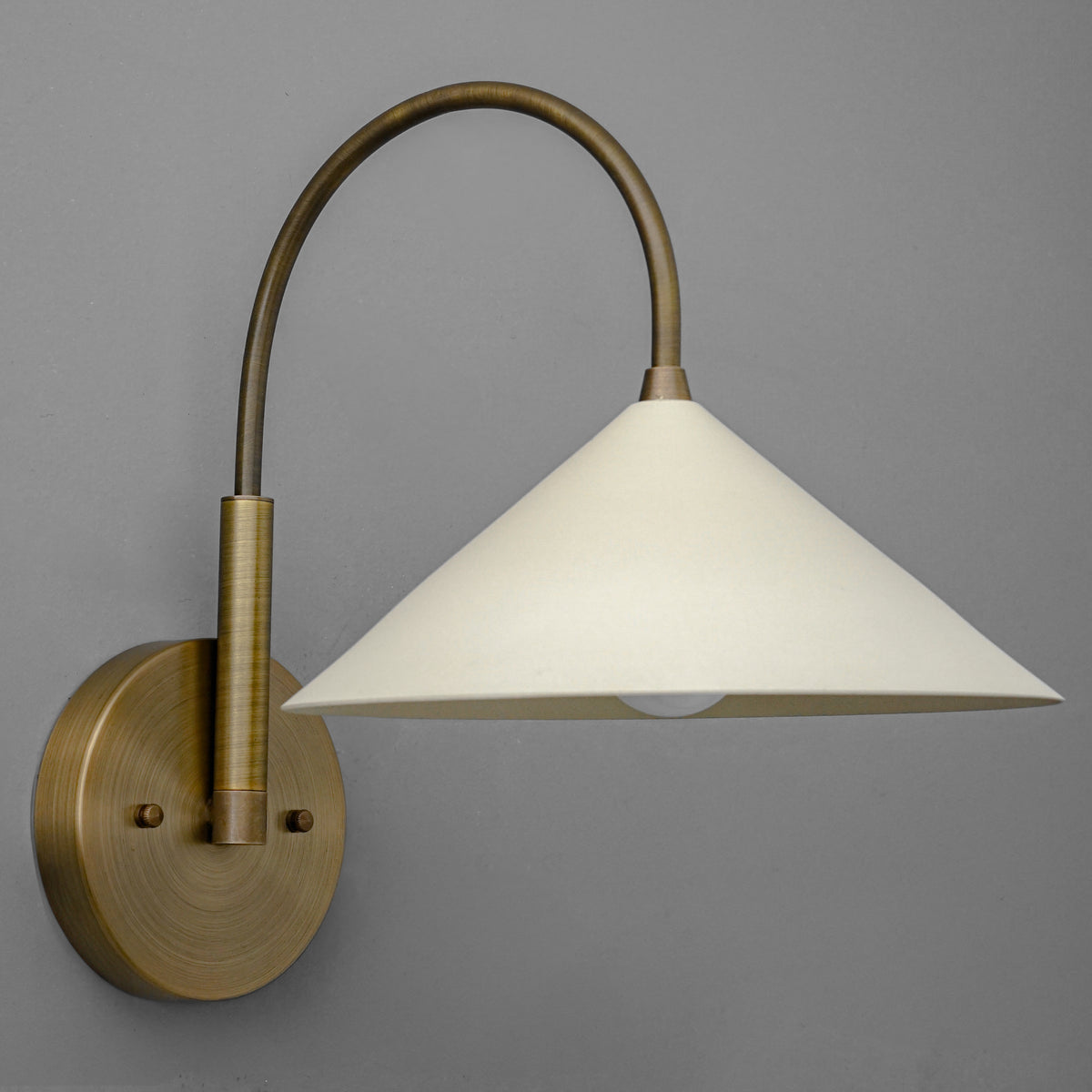 Antique brass sconce with curved arm and cream conical shade against gray background. - Sconce Model No. 1583