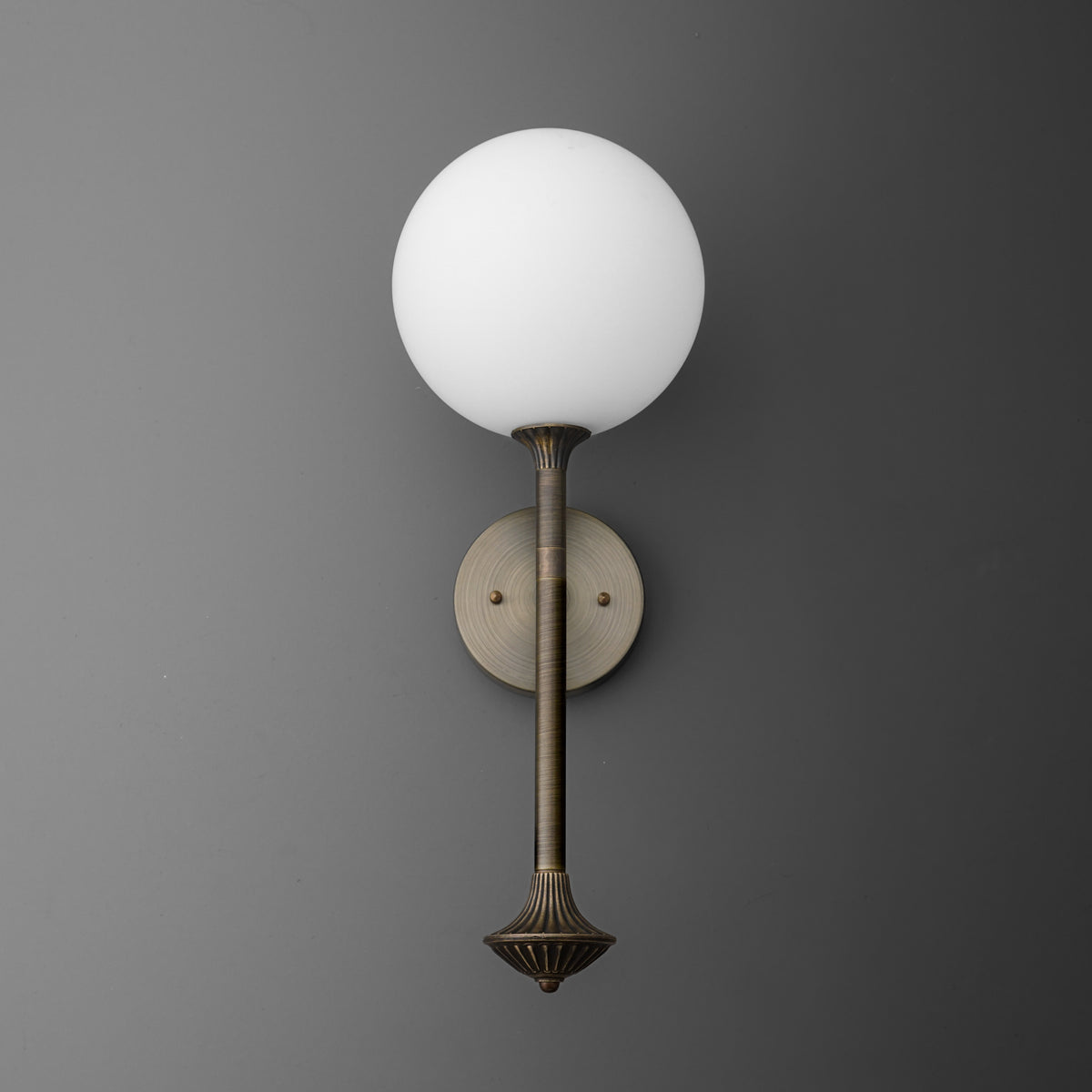 Wall-mounted sconce with an antique brass finish, featuring a round white glass globe shade and a slender vertical arm. - SCONCE MODEL NO. 1059