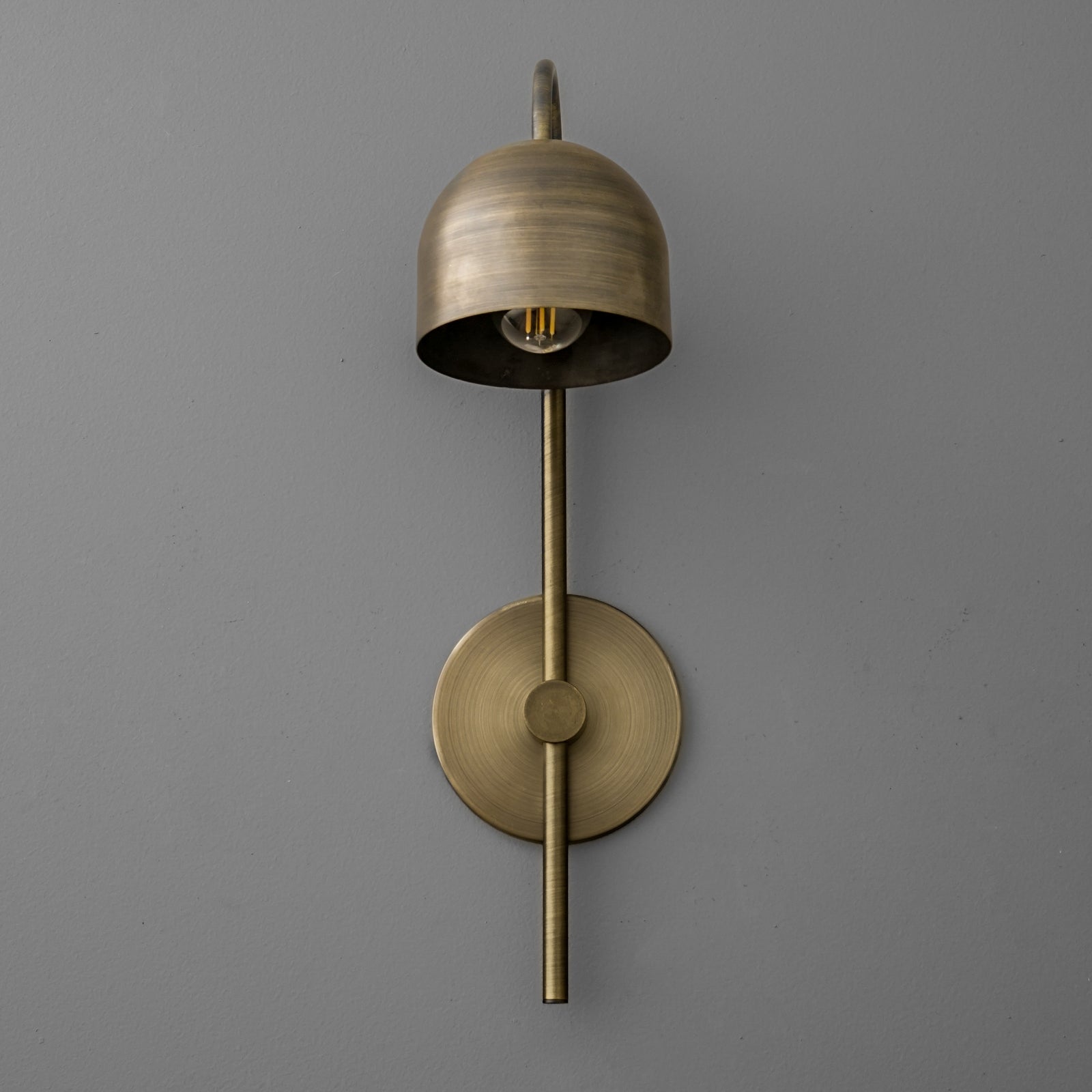 Antique brass sconce with bell-shaped shade and vertical rod mounting on gray wall. - Sconce Model No. 7340