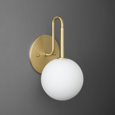Wall sconce with raw brass finish and frosted white glass globe shade against gray background. - SCONCE MODEL NO. 9105