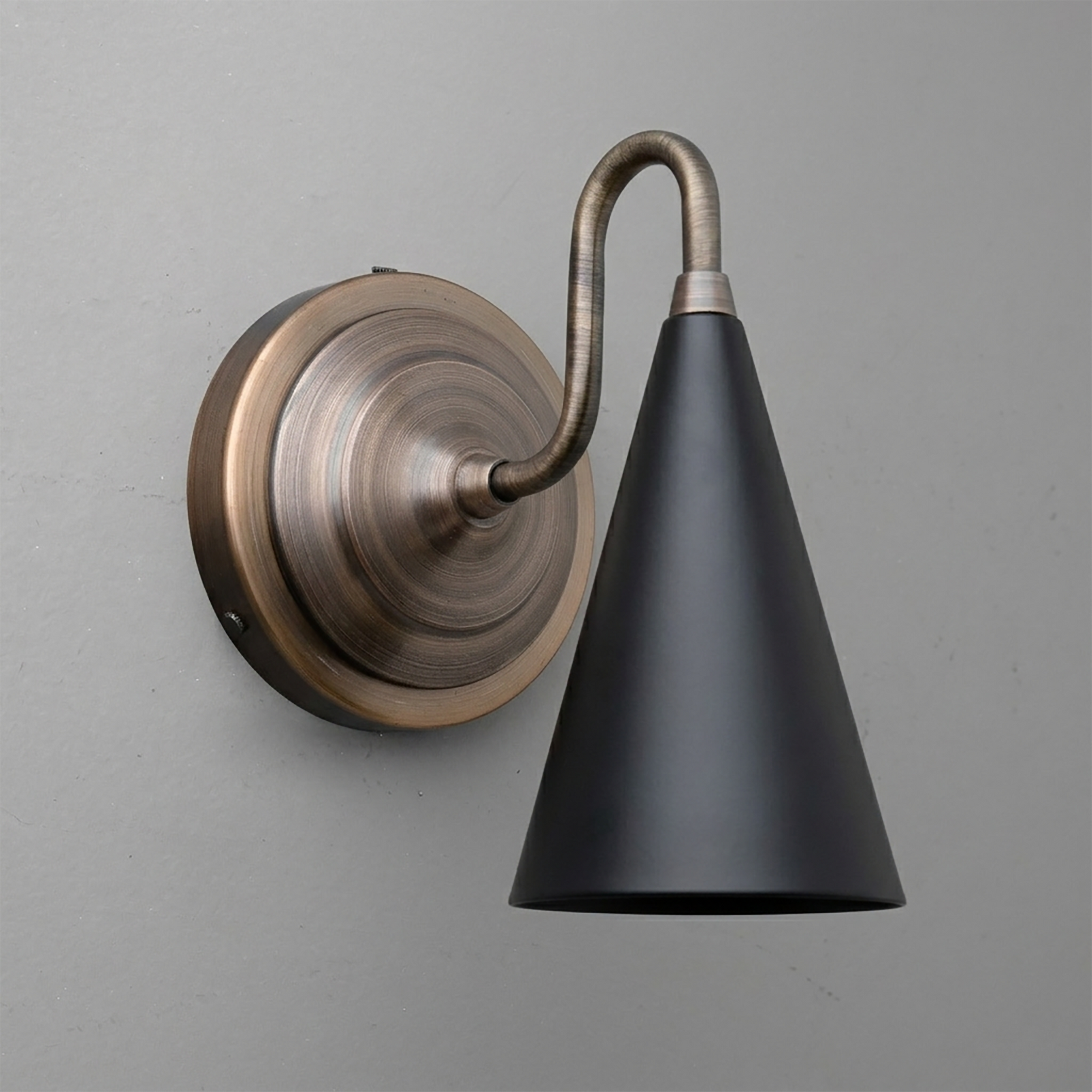 Wall-mounted sconce with aged brass round base and curved arm, featuring matte black conical shade. - Sconce Model No. 6790