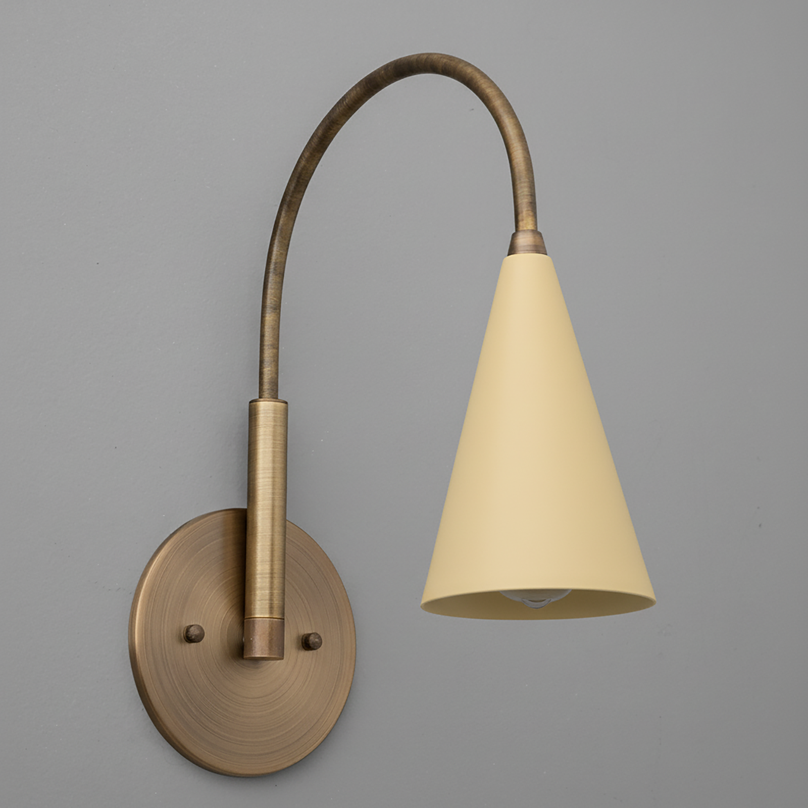 Wall sconce with curved antique brass arm and matte beige conical metal shade. - SCONCE MODEL NO. 1309