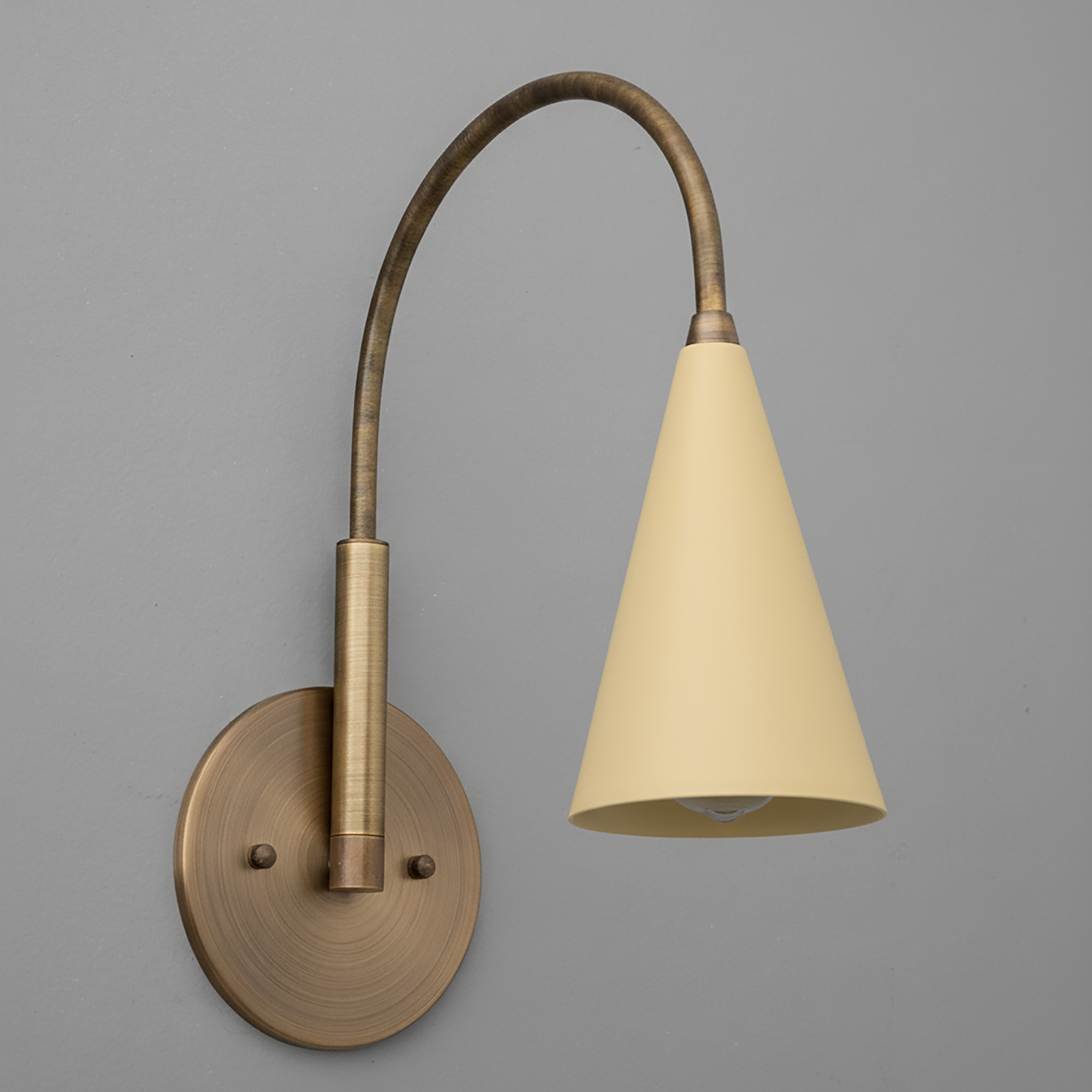Wall sconce with curved antique brass arm and matte beige conical metal shade. - SCONCE MODEL NO. 1309
