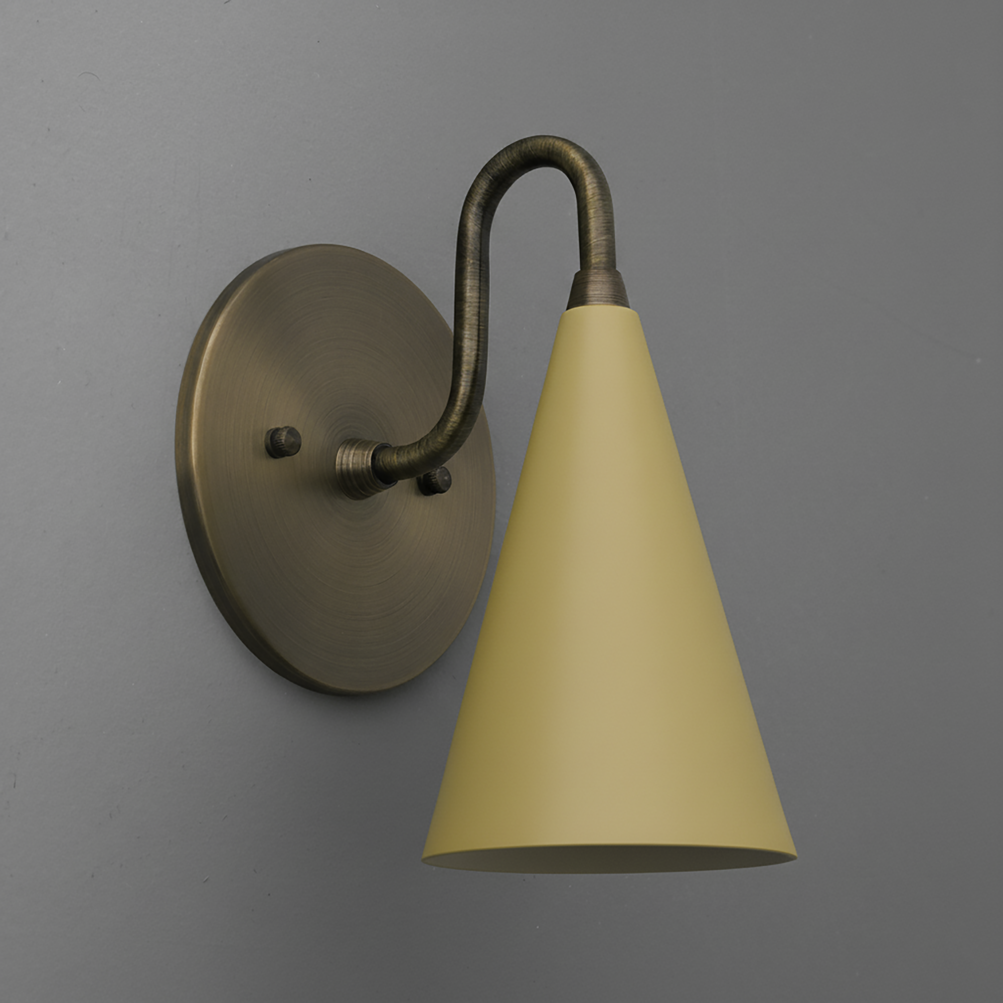 Antique brass wall sconce with a curved arm and yellow conical shade on a gray wall. - Sconce Model No. 2900
