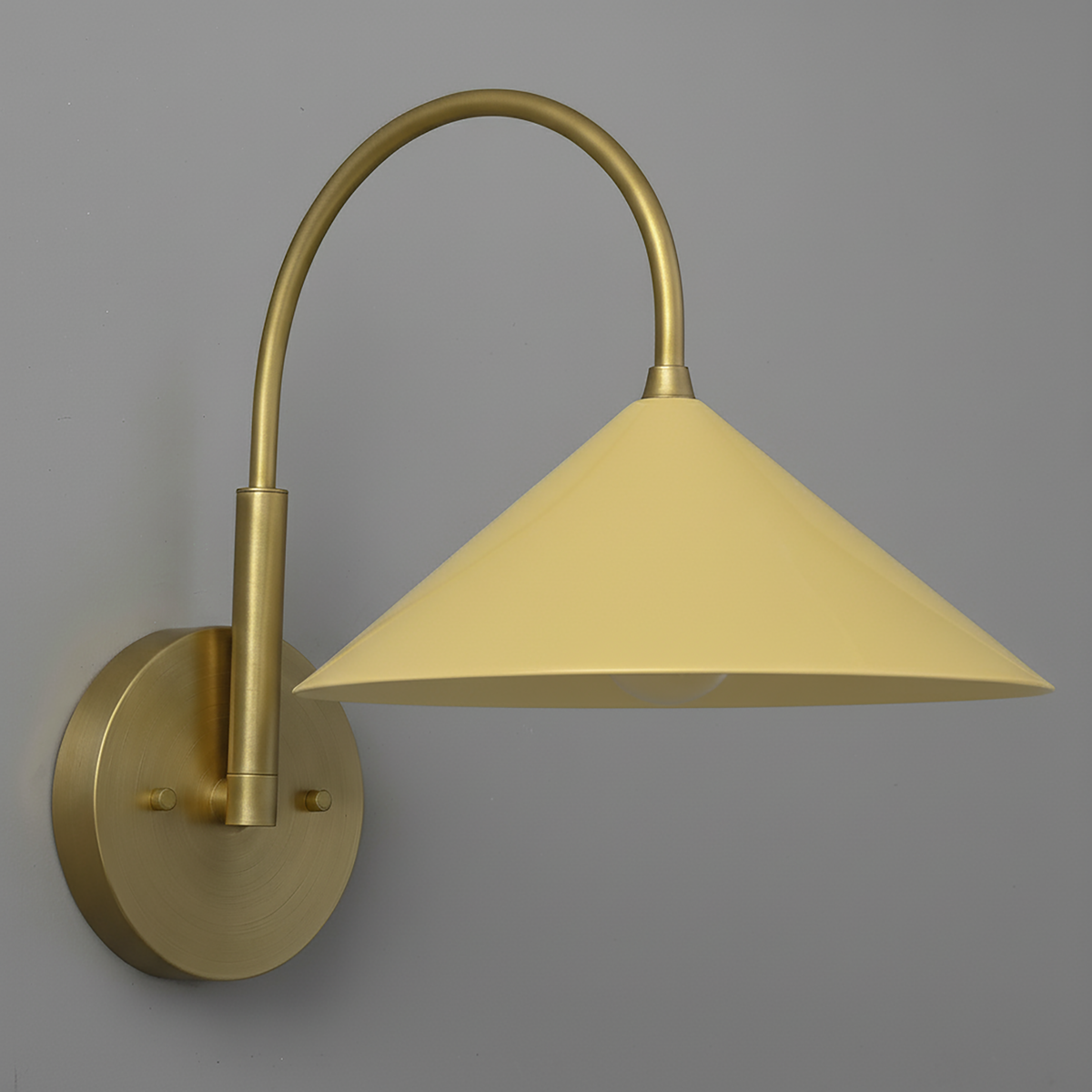 Antique brass sconce with curved arm and yellow conical metal shade against gray background. - Sconce Model No. 1583