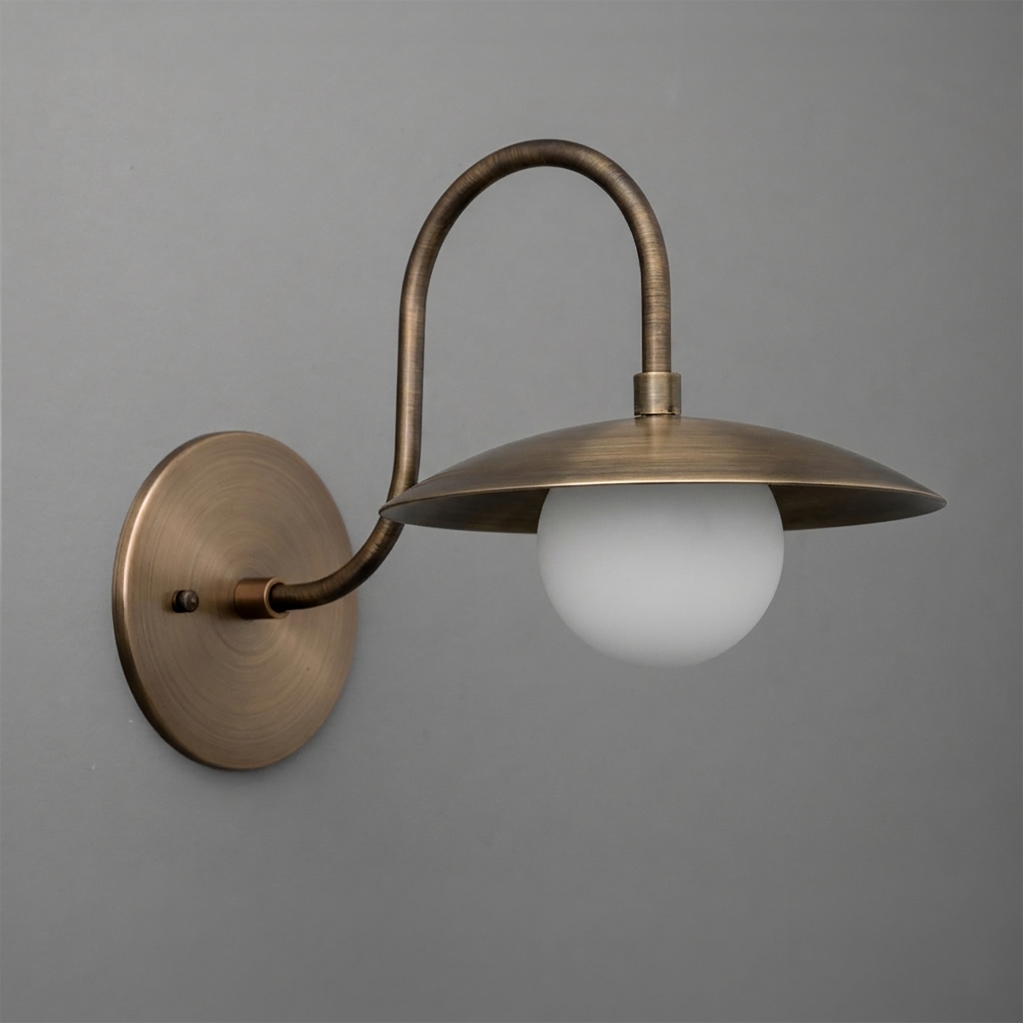 Antique brass wall sconce with curved arm, flat wide metal shade, and frosted globe bulb. - SCONCE MODEL NO. 3799