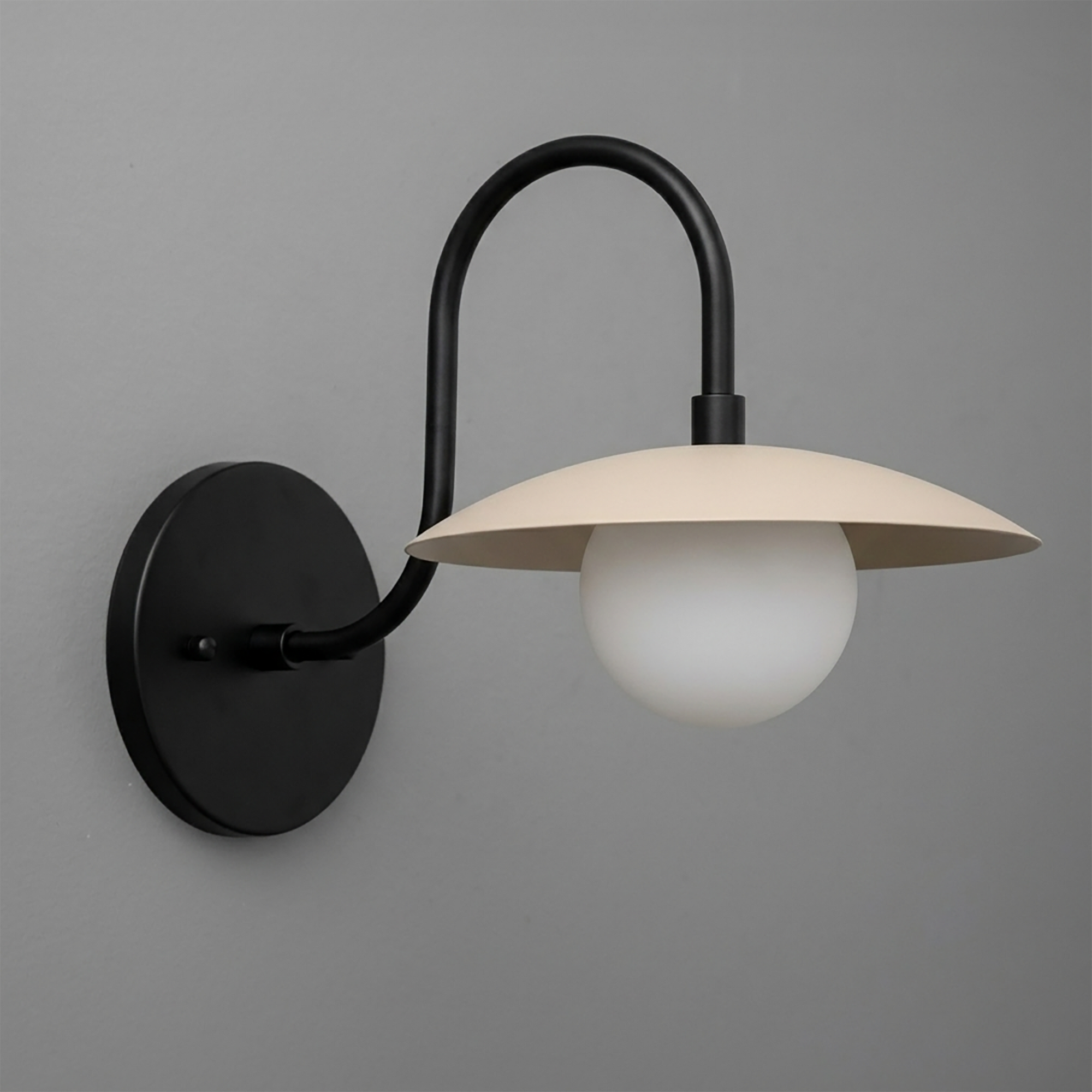 Matte black metal wall sconce with curved arm and cream flat dome shade over white globe bulb. - SCONCE MODEL NO. 3799