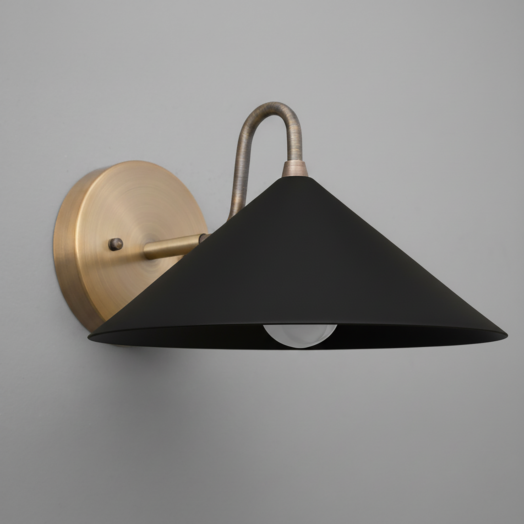 Wall sconce with matte black metal conical shade and antique brass curved arm and round backplate. - SCONCE MODEL NO. 6528