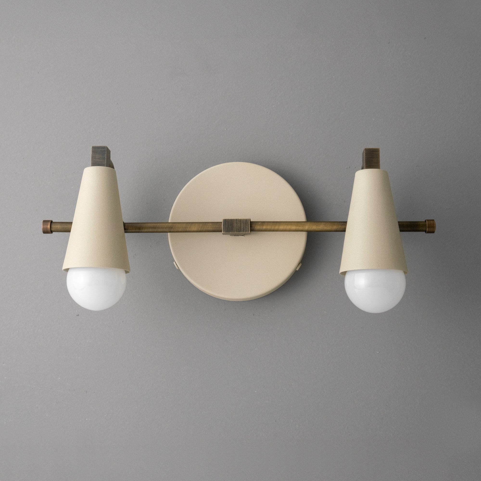 Scandinavian-style vanity light with two white conical shades and exposed round bulbs on a matte beige circular base with. - VANITY LIGHT MODEL NO. 1229
