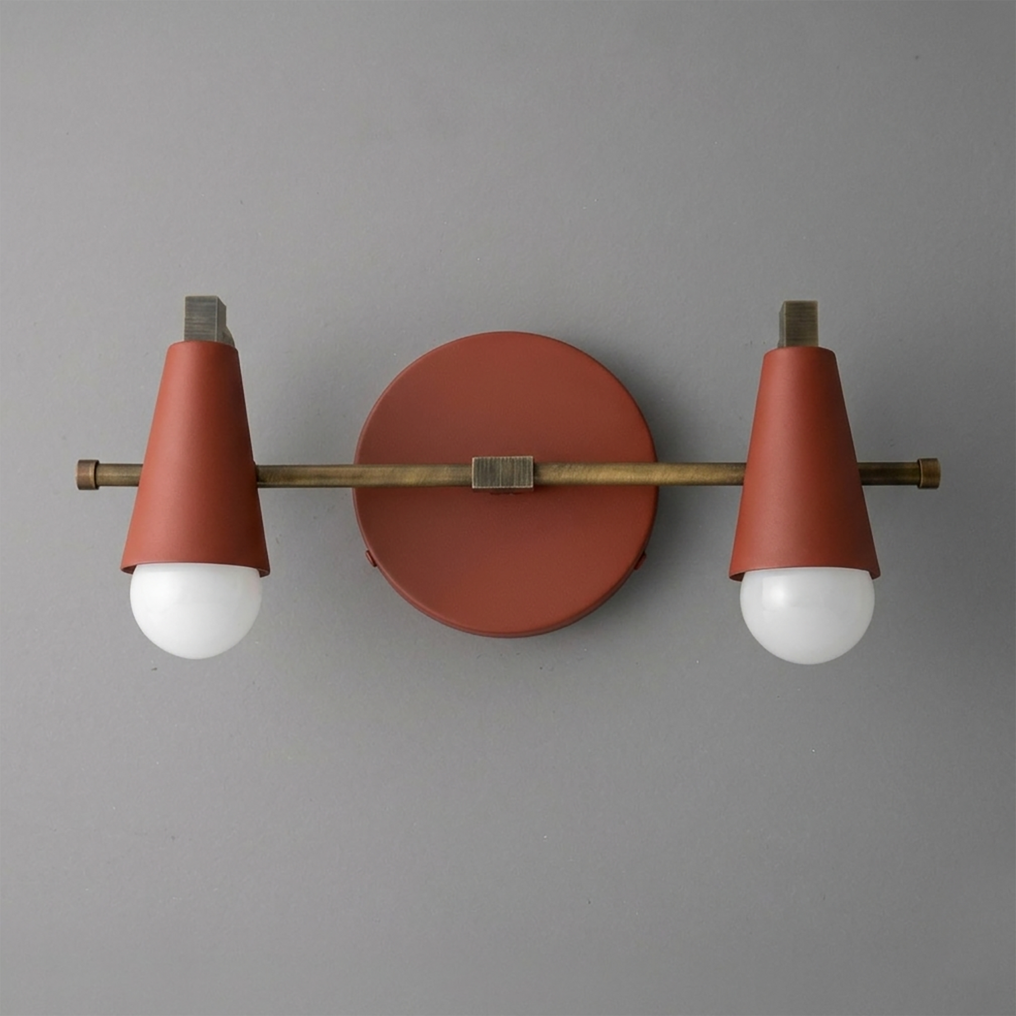 Scandinavian-style 2-bulb vanity light with matte rust-orange conical shades and brass fixture against gray wall. - VANITY LIGHT MODEL NO. 1229