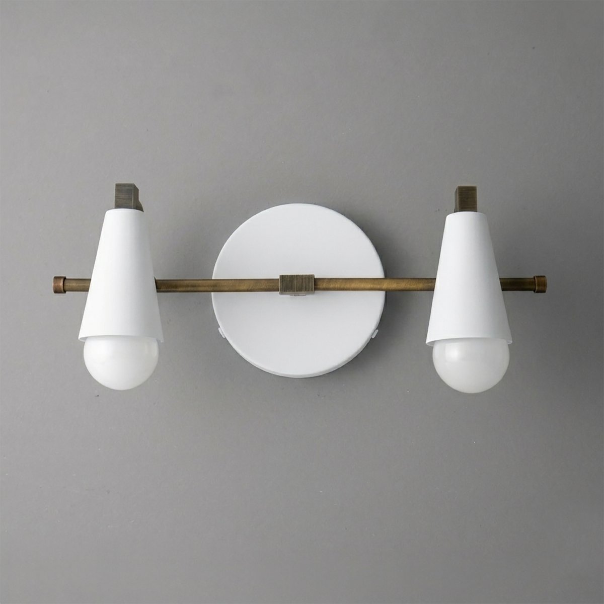Scandinavian-style vanity light with two white cone-shaped shades and round backplate in matte brass finish. - VANITY LIGHT MODEL NO. 1229