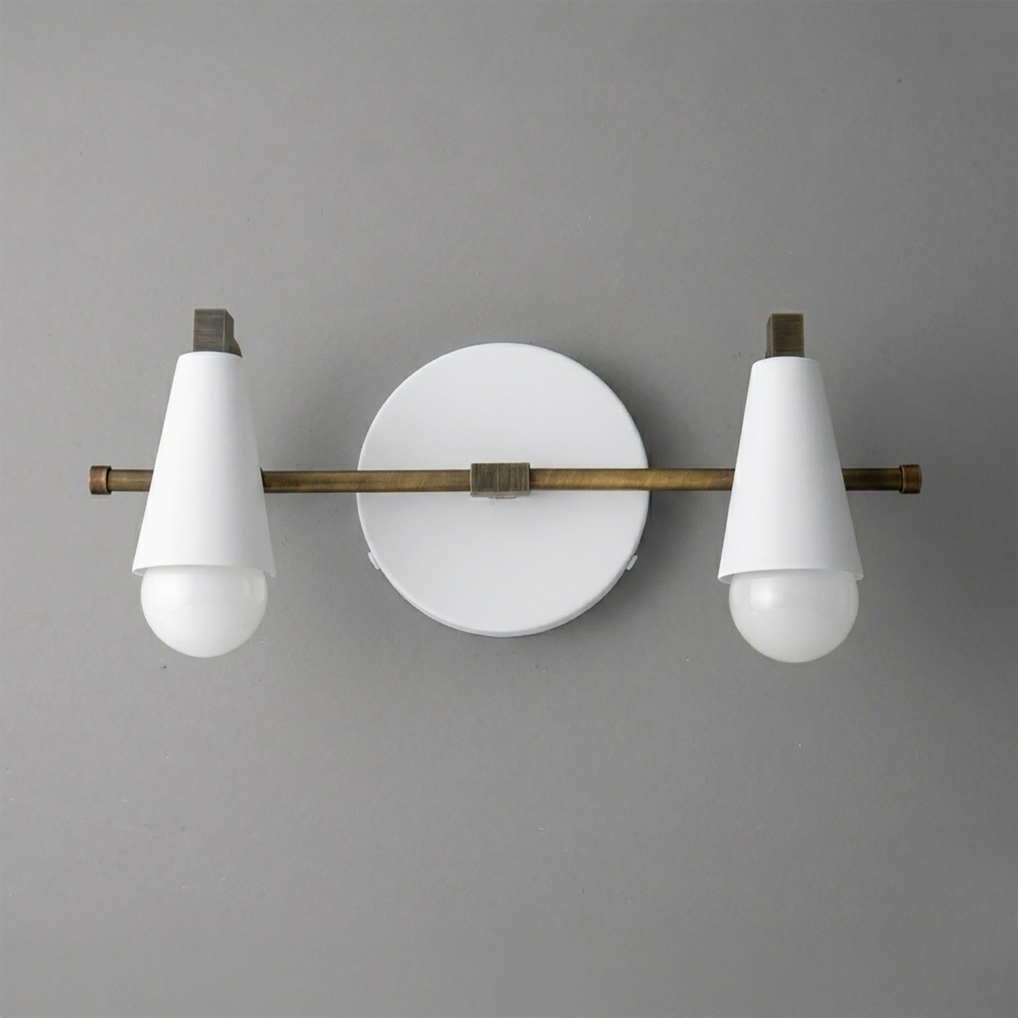 Scandinavian-style vanity light with two white cone-shaped shades and round backplate in matte brass finish. - VANITY LIGHT MODEL NO. 1229