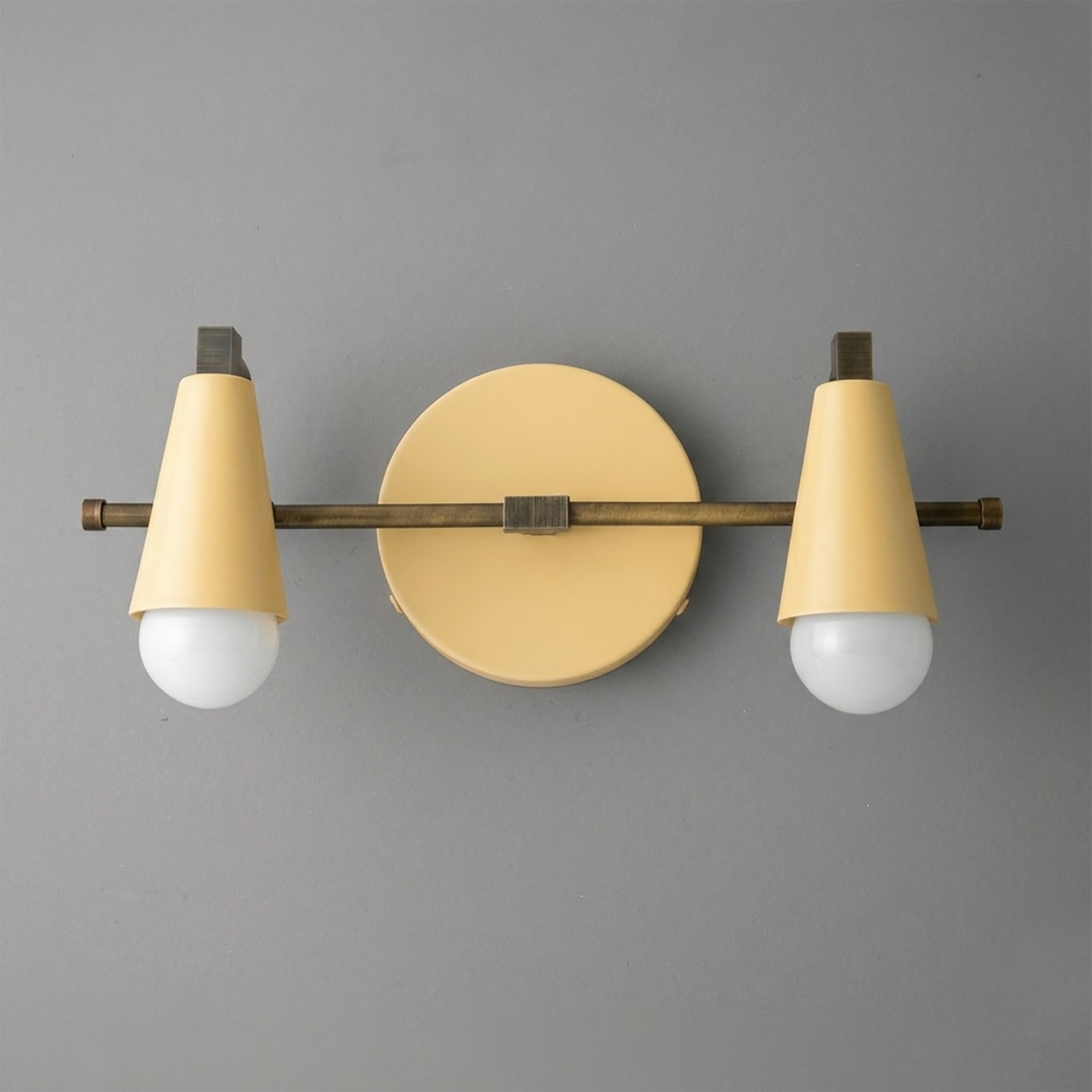 Scandinavian-style vanity light with two cream cone-shaped shades and brass horizontal bar mounting on round backplate. - VANITY LIGHT MODEL NO. 1229