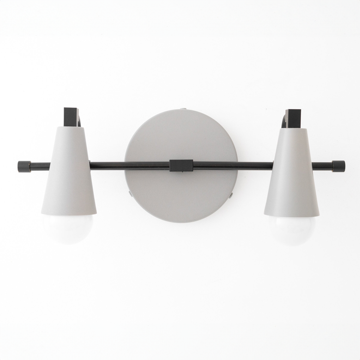 Black metal vanity light with two conical white shades and exposed bulbs mounted on a round backplate. - VANITY LIGHT MODEL NO. 1229