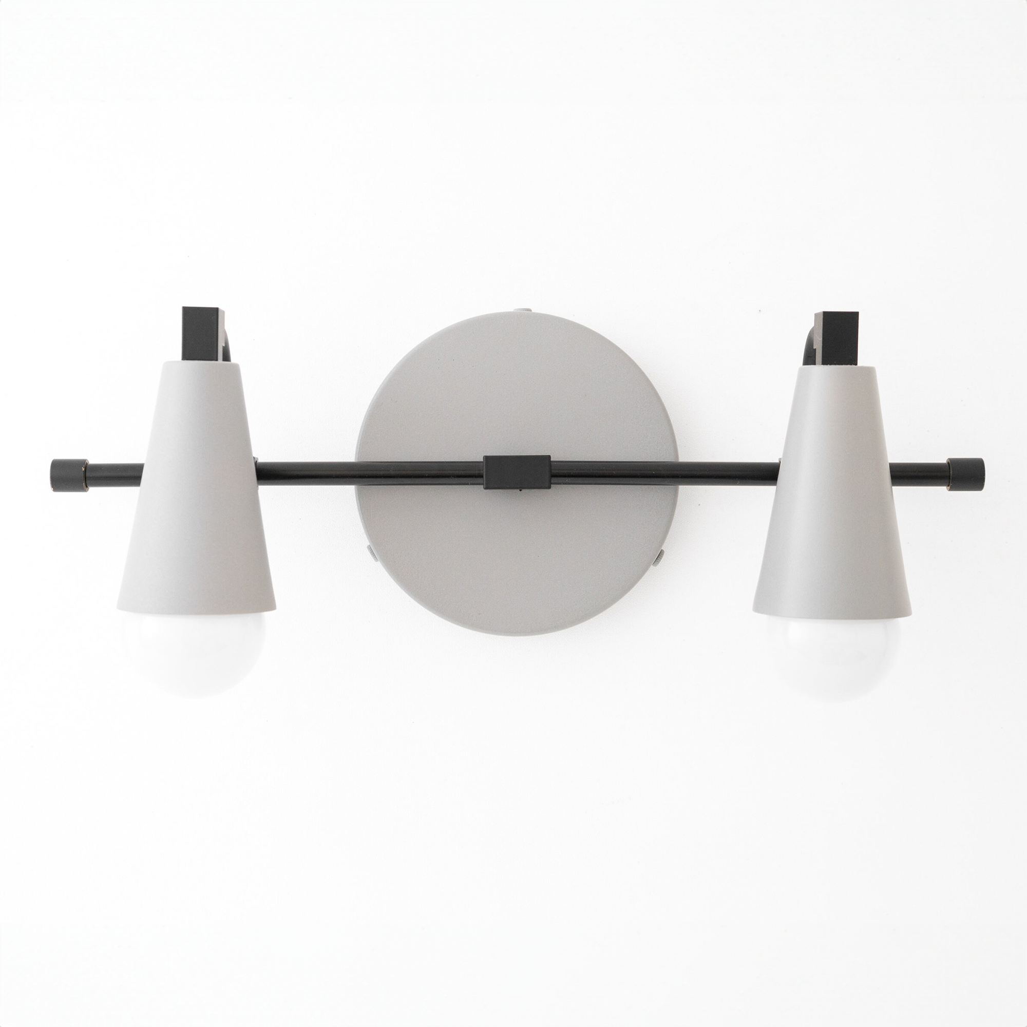 Black metal vanity light with two conical white shades and exposed bulbs mounted on a round backplate. - VANITY LIGHT MODEL NO. 1229