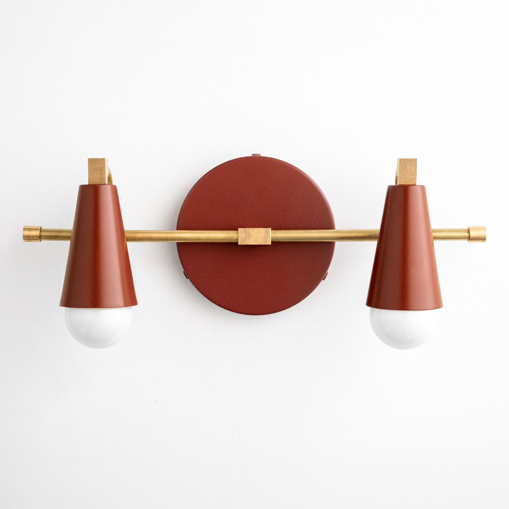 Scandinavian style vanity light with two rust-red conical shades and a brass horizontal rod mounted on a round base. - VANITY LIGHT MODEL NO. 1229