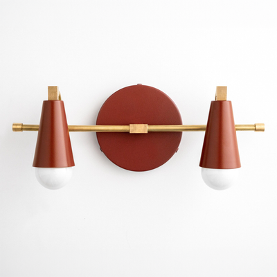 Scandinavian style vanity light with two rust-red conical shades and a brass horizontal rod mounted on a round base. - VANITY LIGHT MODEL NO. 1229