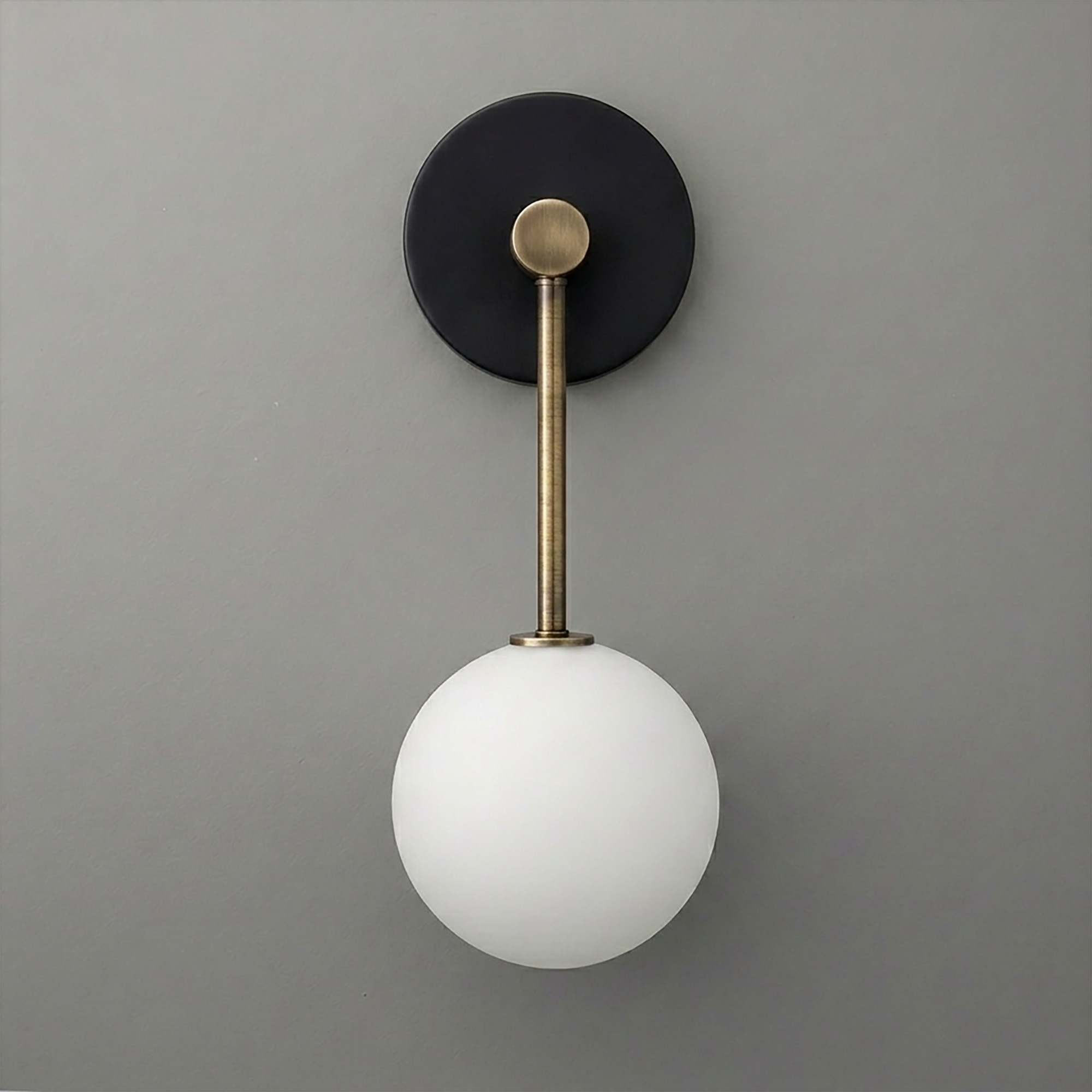 Wall sconce with matte black circular base, brass rod, and frosted white globe bulb shade. - Sconce Model No. 5999