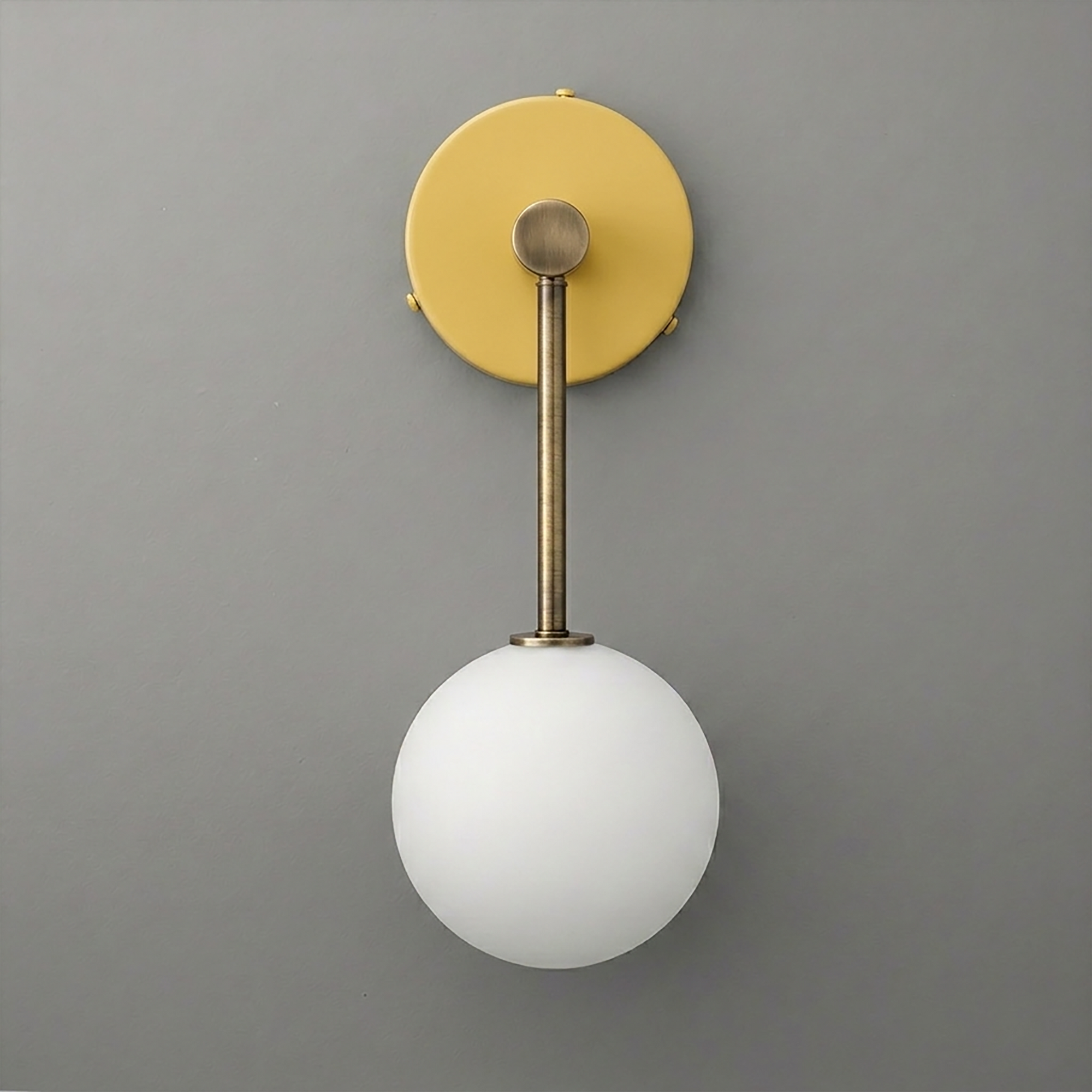 Wall sconce with matte brass fixture and round white frosted glass globe shade on gray background. - Sconce Model No. 5999