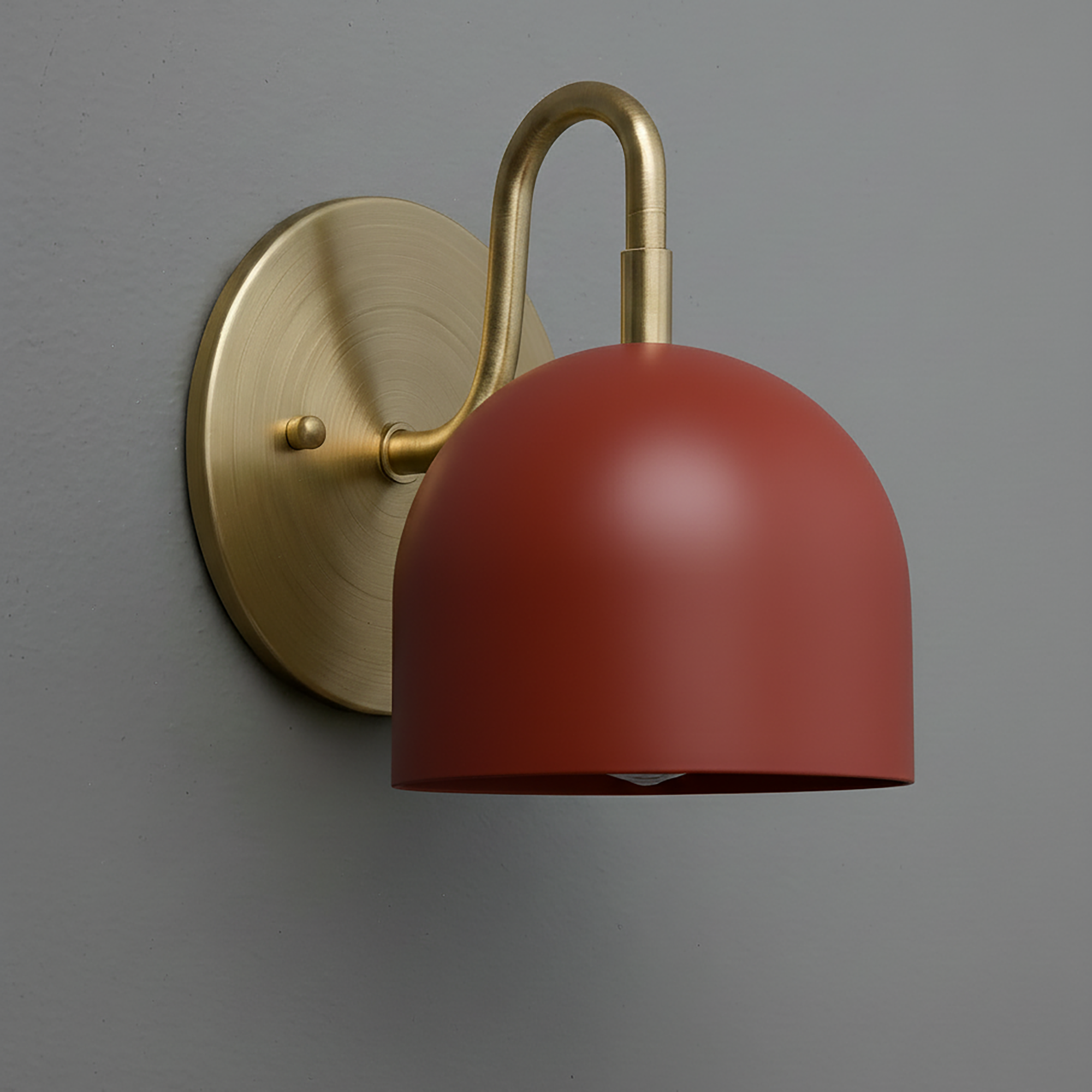 Wall sconce with antique brass finish and smooth brick red dome shade against gray wall. - Sconce Model No. 5416
