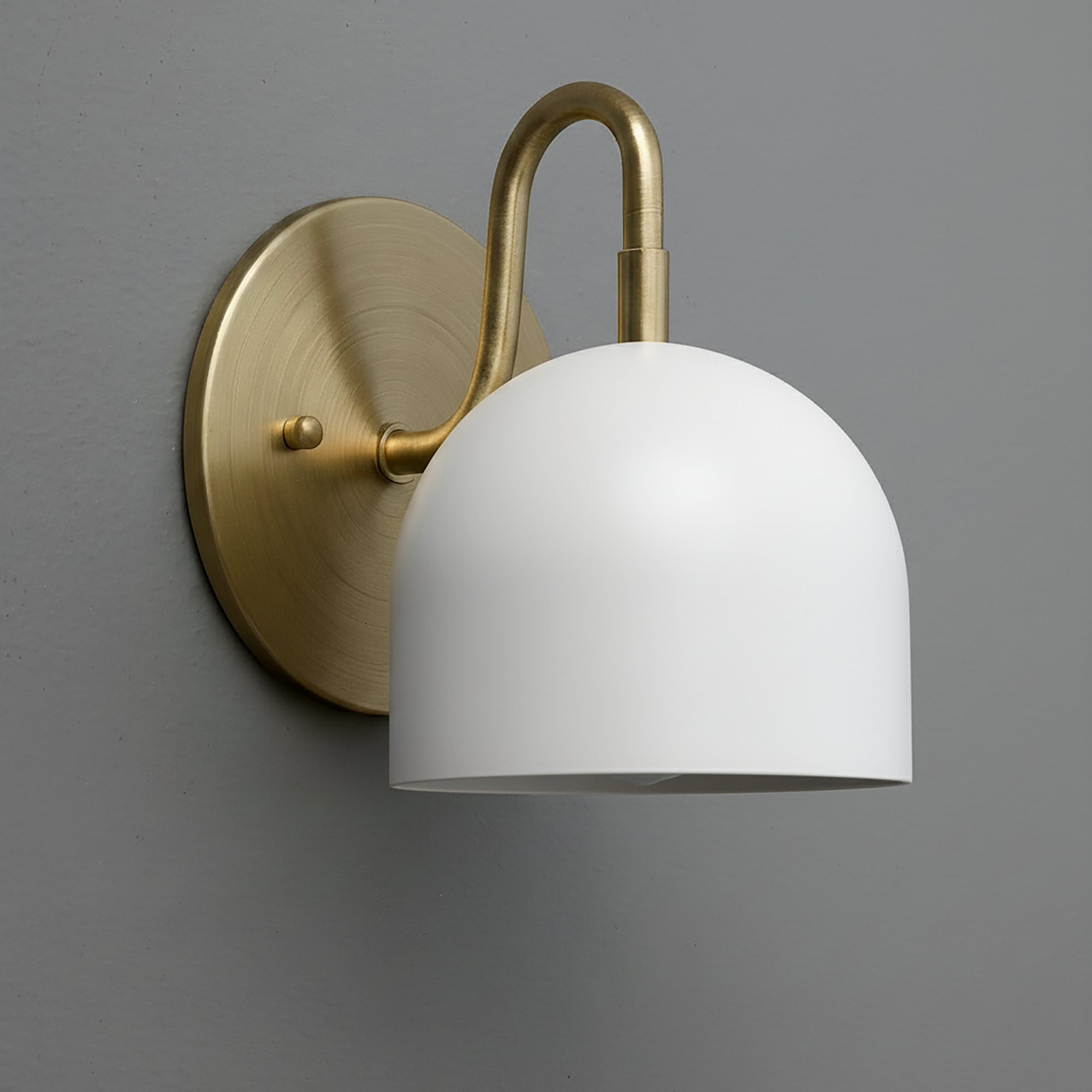 Brushed brass wall sconce with curved arm and matte white dome-shaped shade against gray wall. - Sconce Model No. 5416