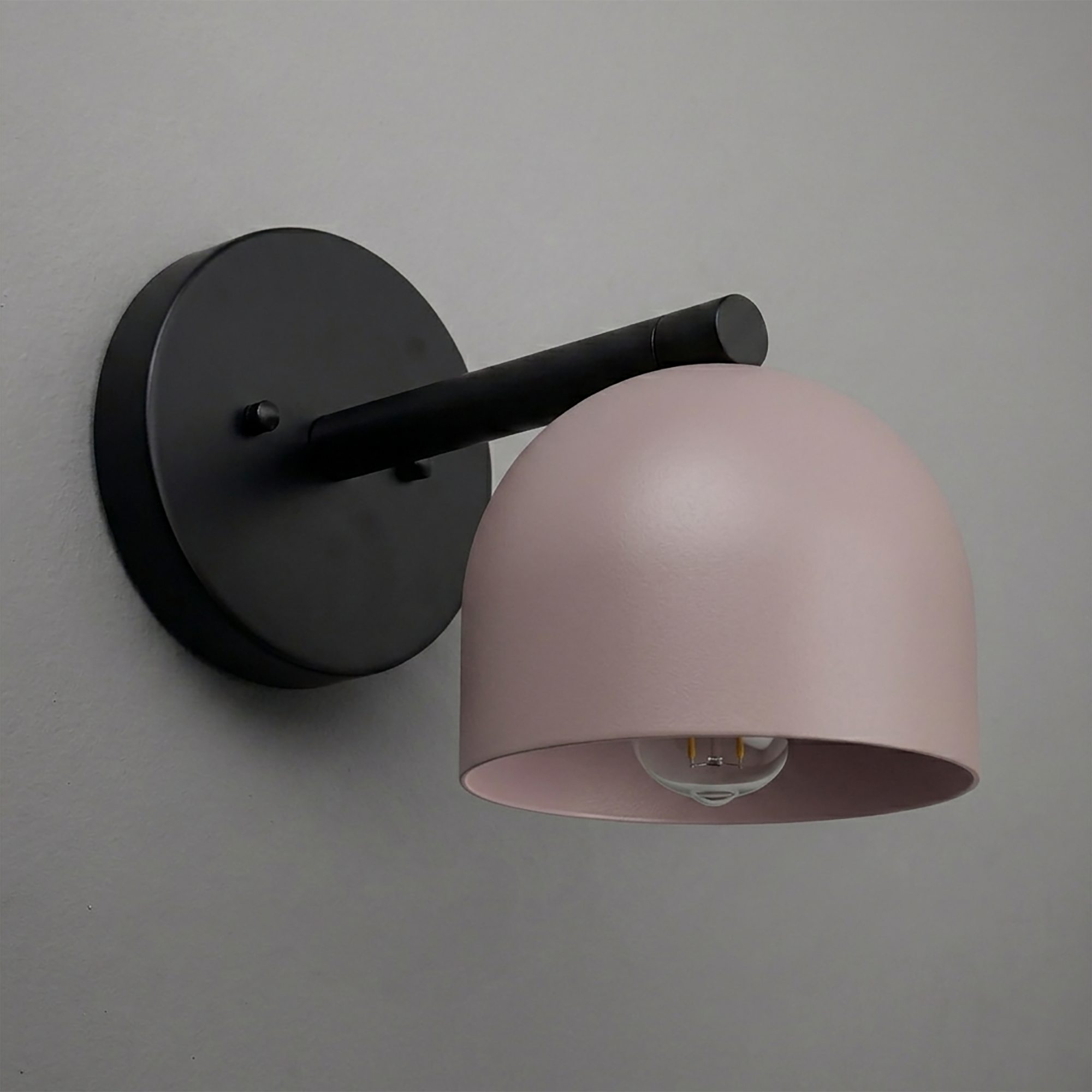 Matte black wall sconce with a single curved arm and a smooth, light pink dome-shaped shade. - Sconce Model No. 5356