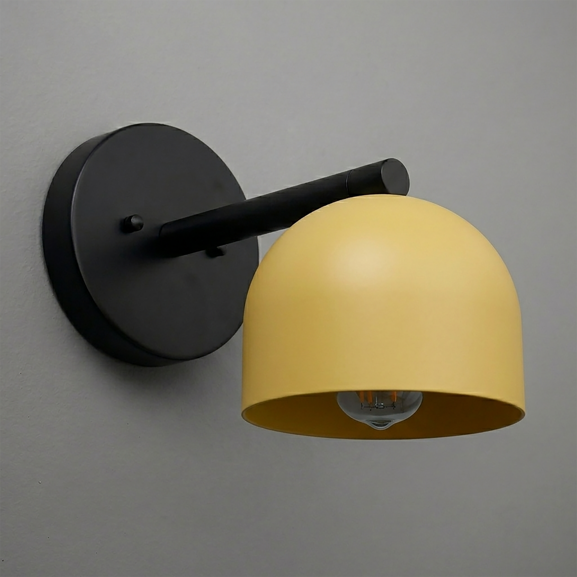 Black matte metal wall sconce with a yellow dome-shaped shade and exposed bulb underneath. - Sconce Model No. 5356