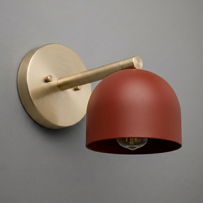 Wall sconce with brushed brass arm and round base, featuring a matte rust-red dome shade and exposed bulb. - Sconce Model No. 5356