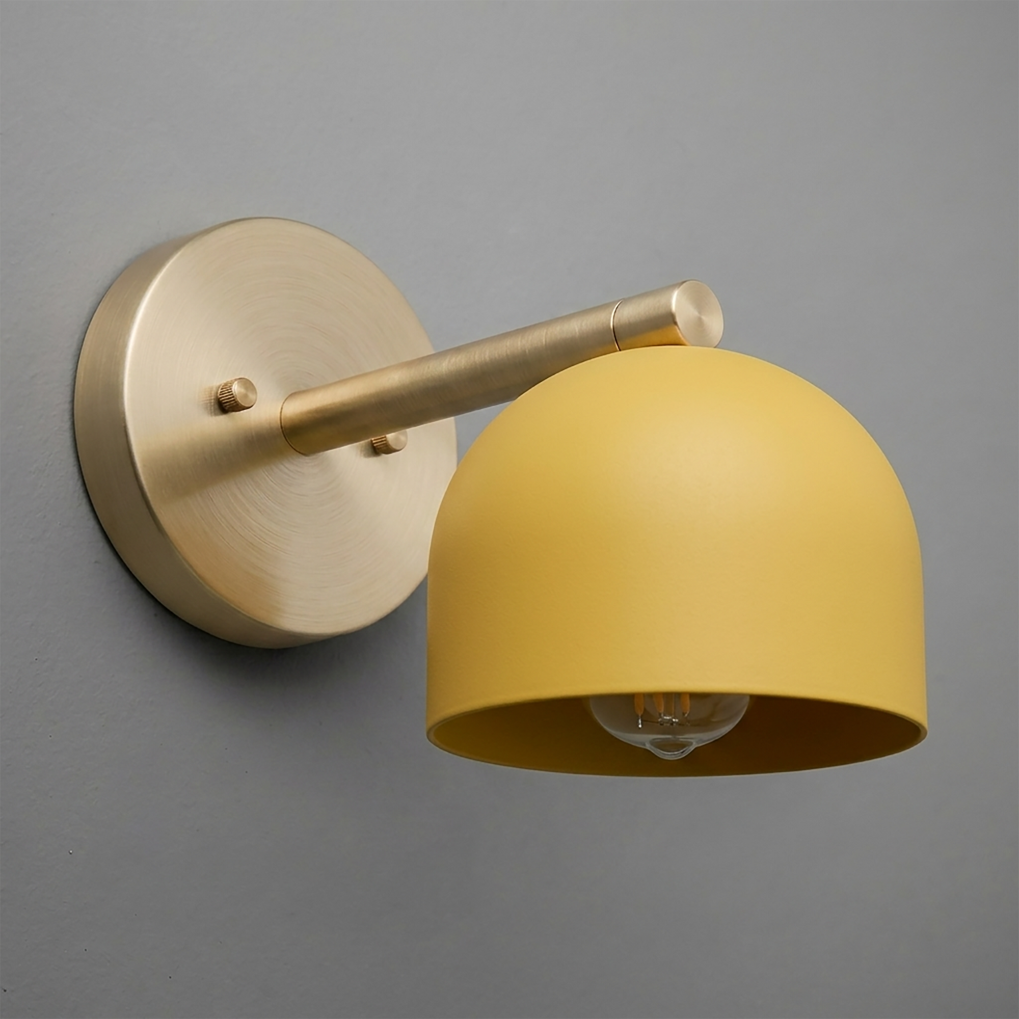 Brushed brass wall sconce with a matte yellow dome-shaped metal shade and exposed bulb. - Sconce Model No. 5356