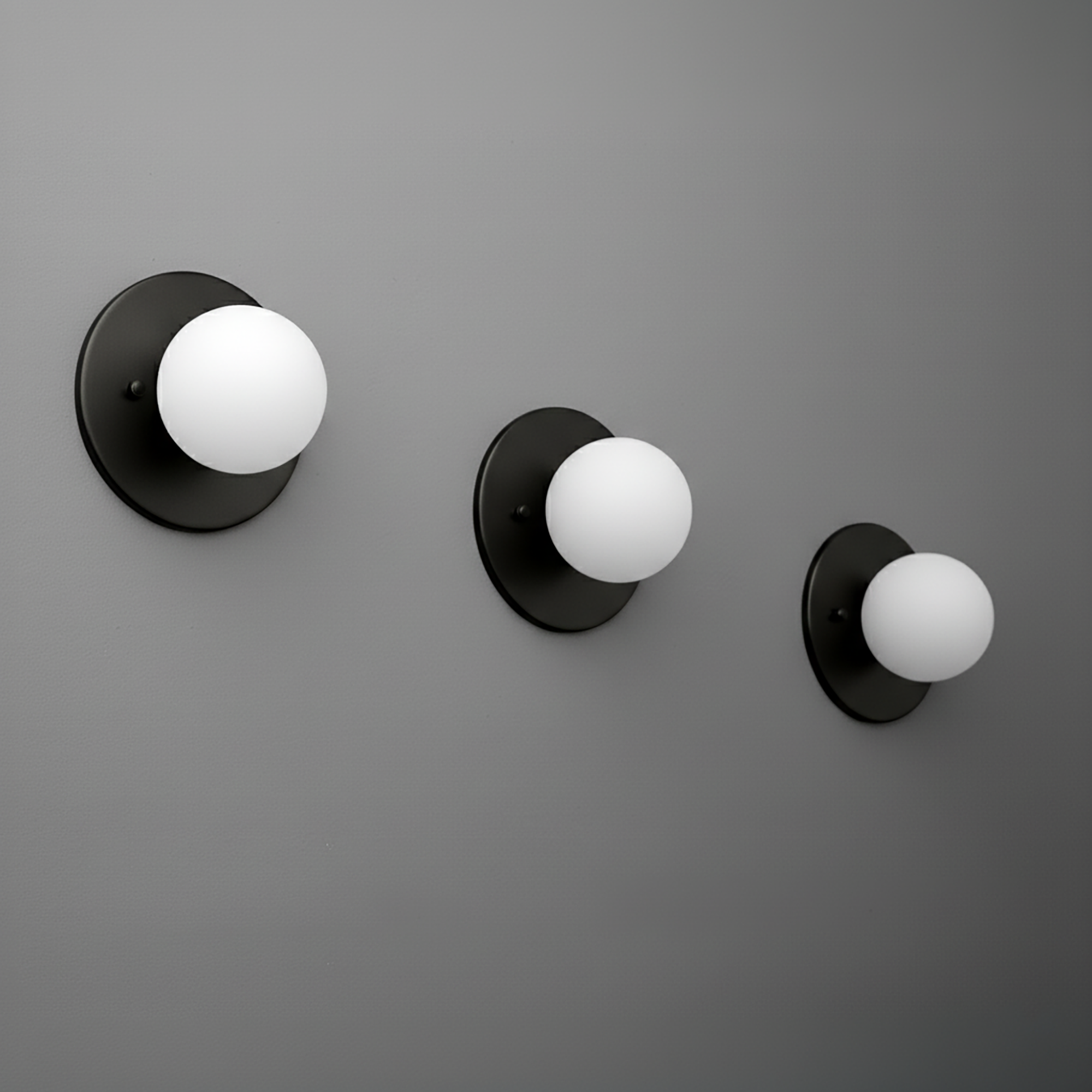 Set of three black metal sconces with white globe shades in small, medium, and large sizes mounted on a gray wall. - Sconce Model No. 5206