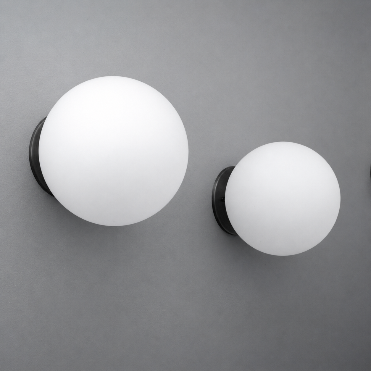 Two white frosted glass globe sconces with black wall mounts, one larger and one smaller, minimalist design. - Sconce Model No. 5206