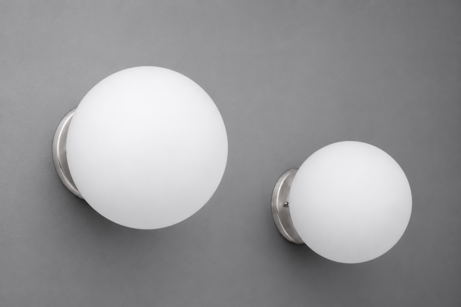 Two white frosted glass globe wall sconces with brushed nickel bases mounted on a gray wall. - Sconce Model No. 5206