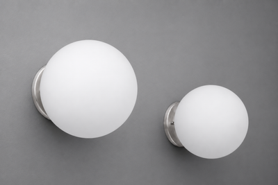 Two white frosted glass globe wall sconces with brushed nickel bases mounted on a gray wall. - Sconce Model No. 5206
