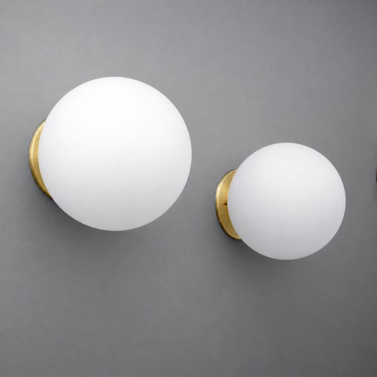 Two white frosted glass globe wall sconces with brushed brass mounts on a gray wall. - Sconce Model No. 5206