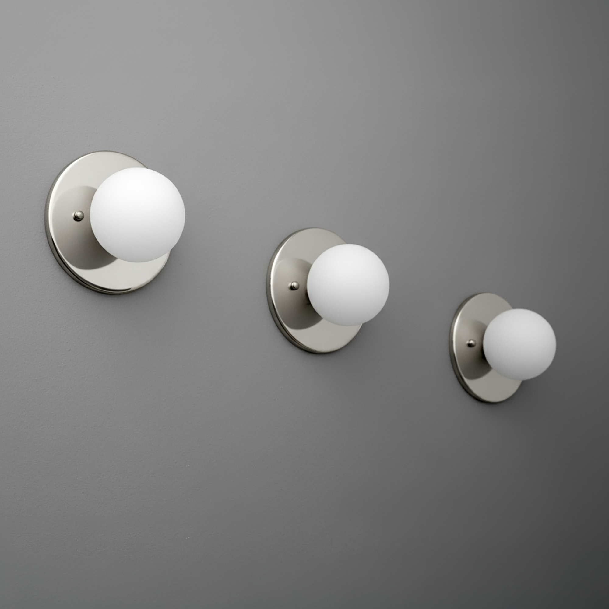 Three brushed nickel sconces with frosted white 3-inch globe shades mounted on a gray wall. - Sconce Model No. 5206