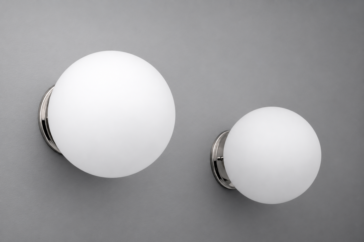 Two spherical white frosted glass wall sconces with polished chrome circular bases, one larger than the other, mounted on. - Sconce Model No. 5206