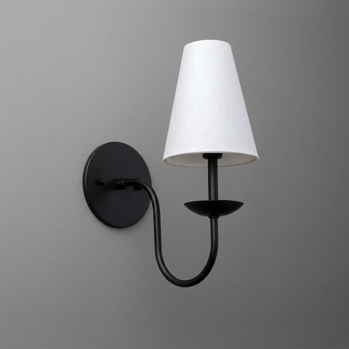 Black metal single-arm wall sconce with white tapered fabric shade and round backplate. - SCONCE MODEL NO. 7085