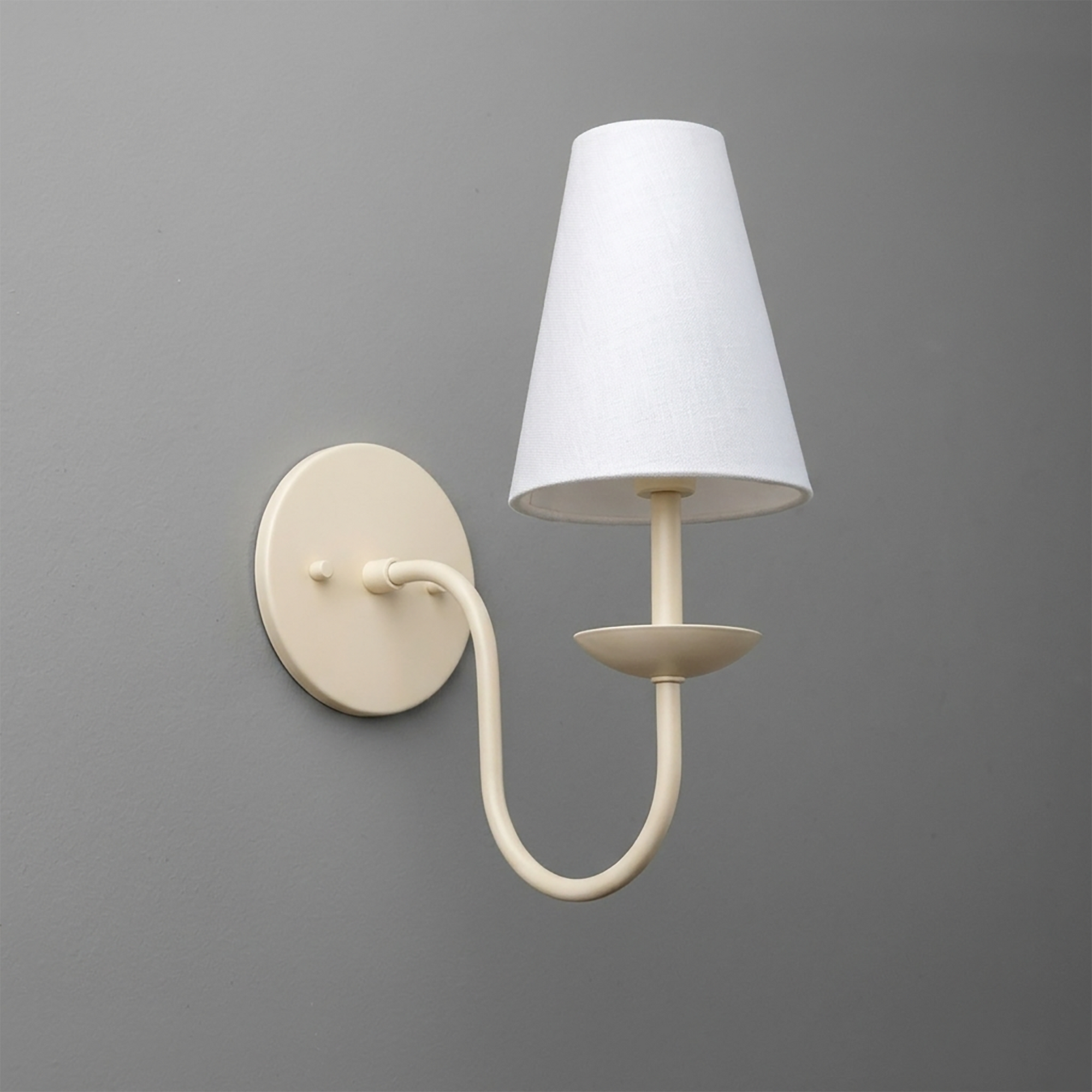 Cream-colored metal wall sconce with curved arm and white tapered fabric shade. - SCONCE MODEL NO. 7085